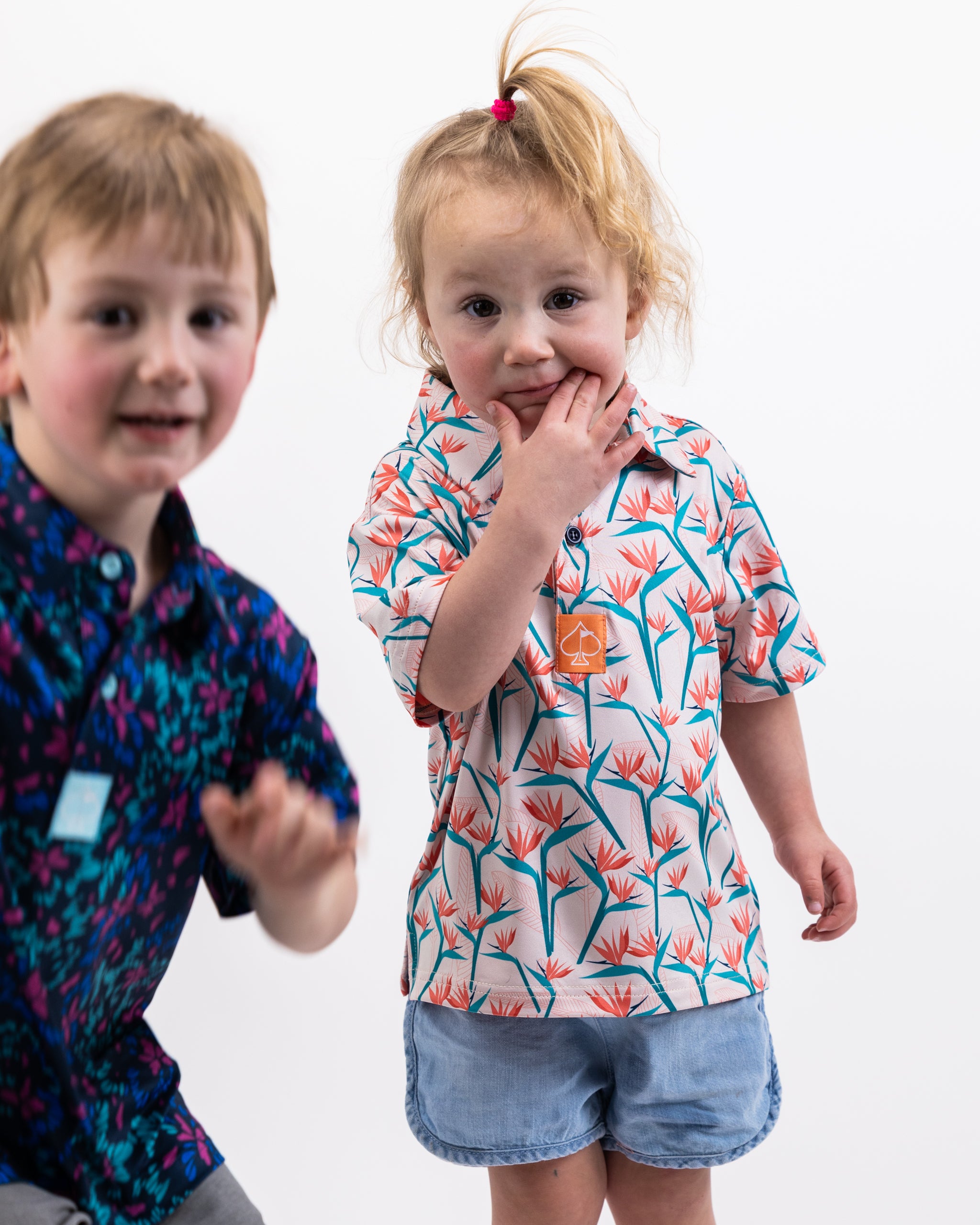 Youth Birds of Paradise shirt featuring vibrant tropical designs on a light background, displayed on a wooden surface.