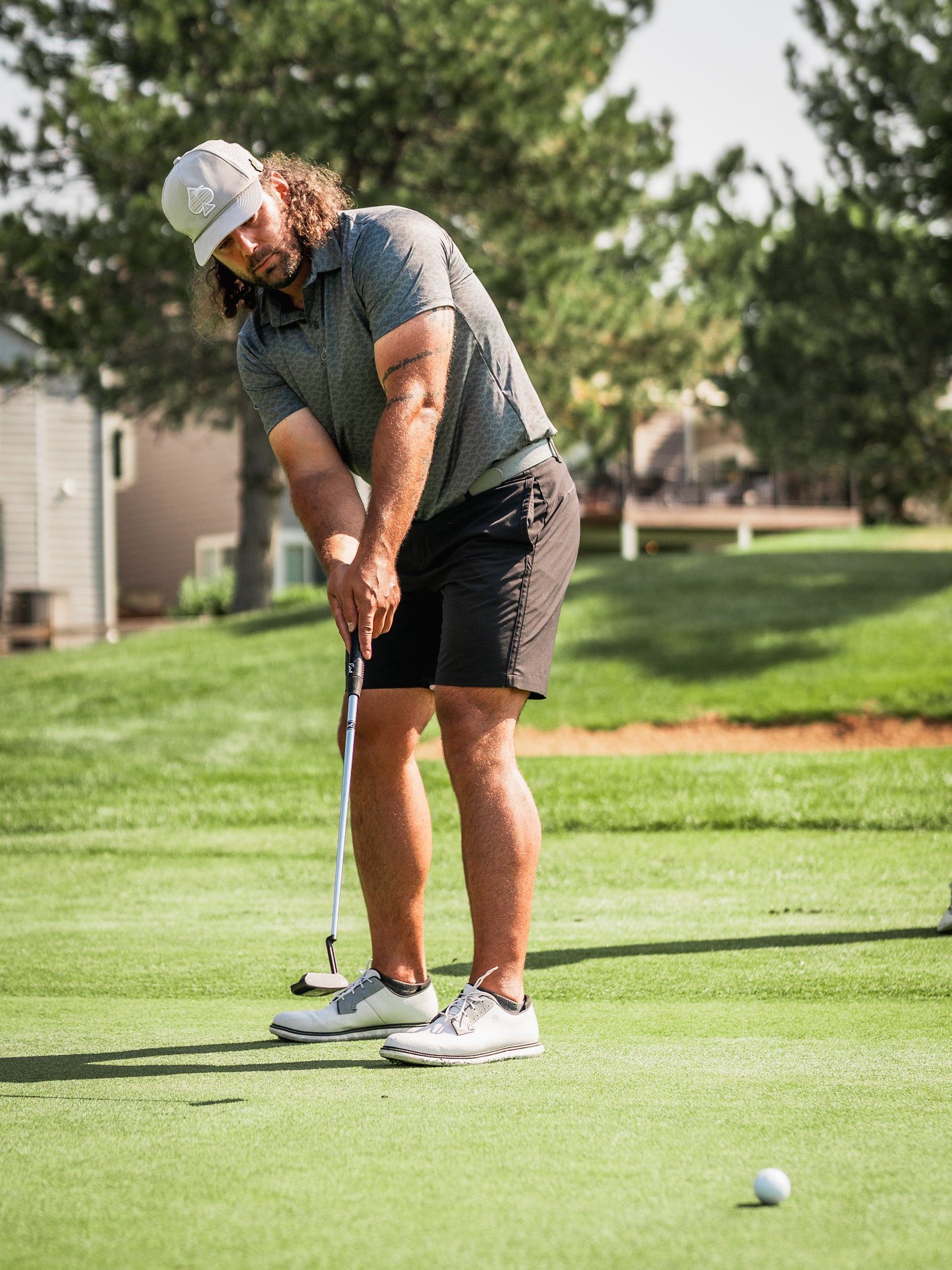 Golfer in a gray polo and black shorts putting on the green, showcasing a focused stance and a Large Mouth headcover nearby.