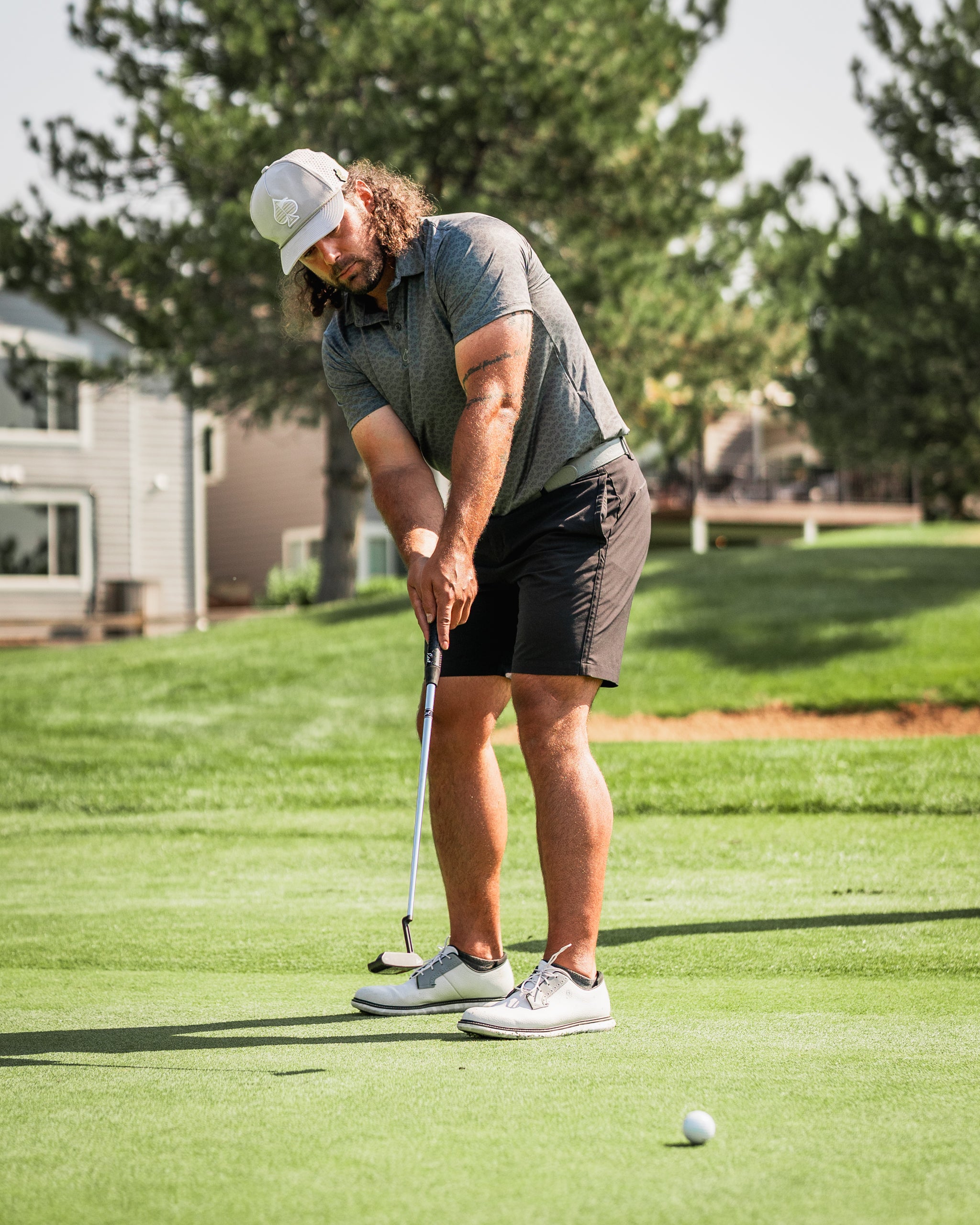 Golfer in a gray polo and black shorts putting on the green, showcasing the Large Mouth headcover in the background.