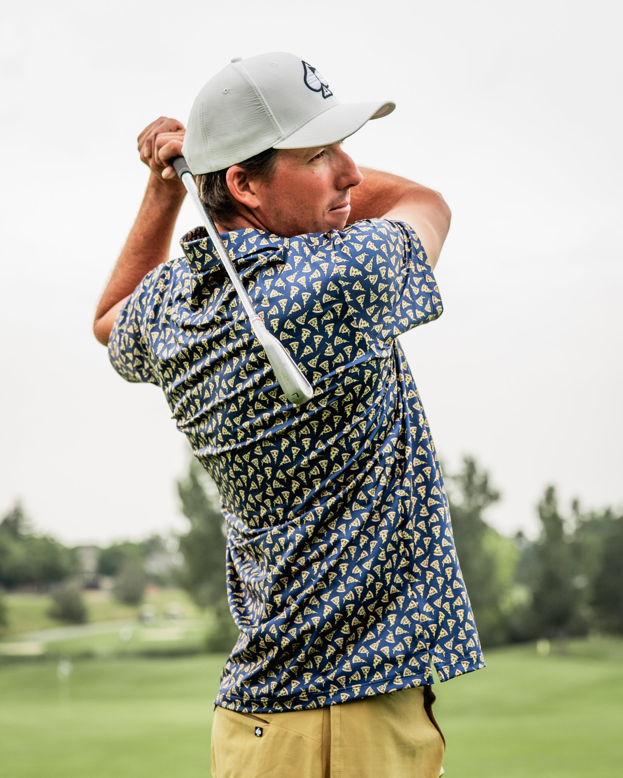 Golfer in a pizza-patterned shirt swings a club on a lush golf course, showcasing bold and unique apparel.