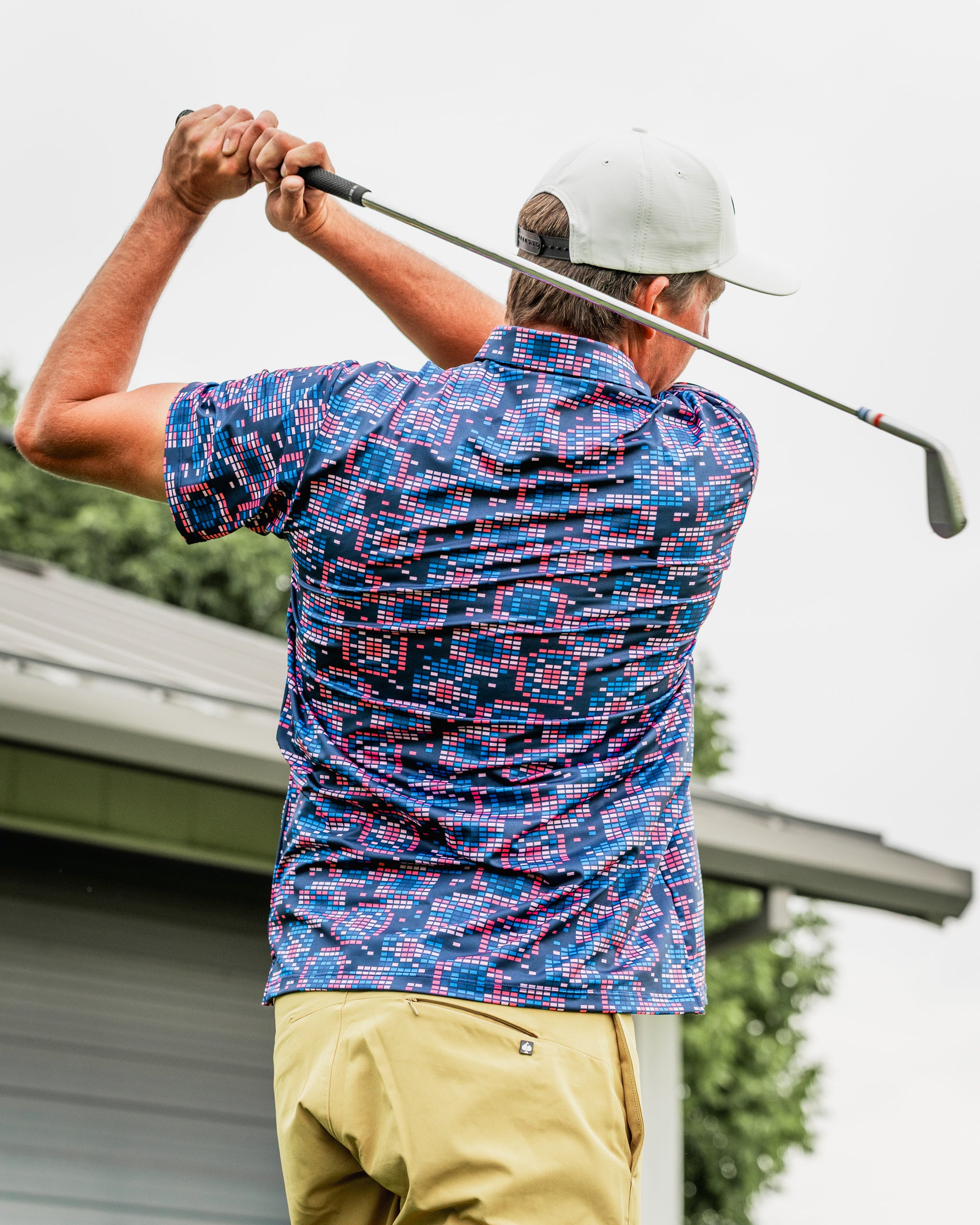 A golfer swings a club while wearing a vibrant Tetrafloral Dark shirt featuring a bold floral pattern in shades of blue and pink.