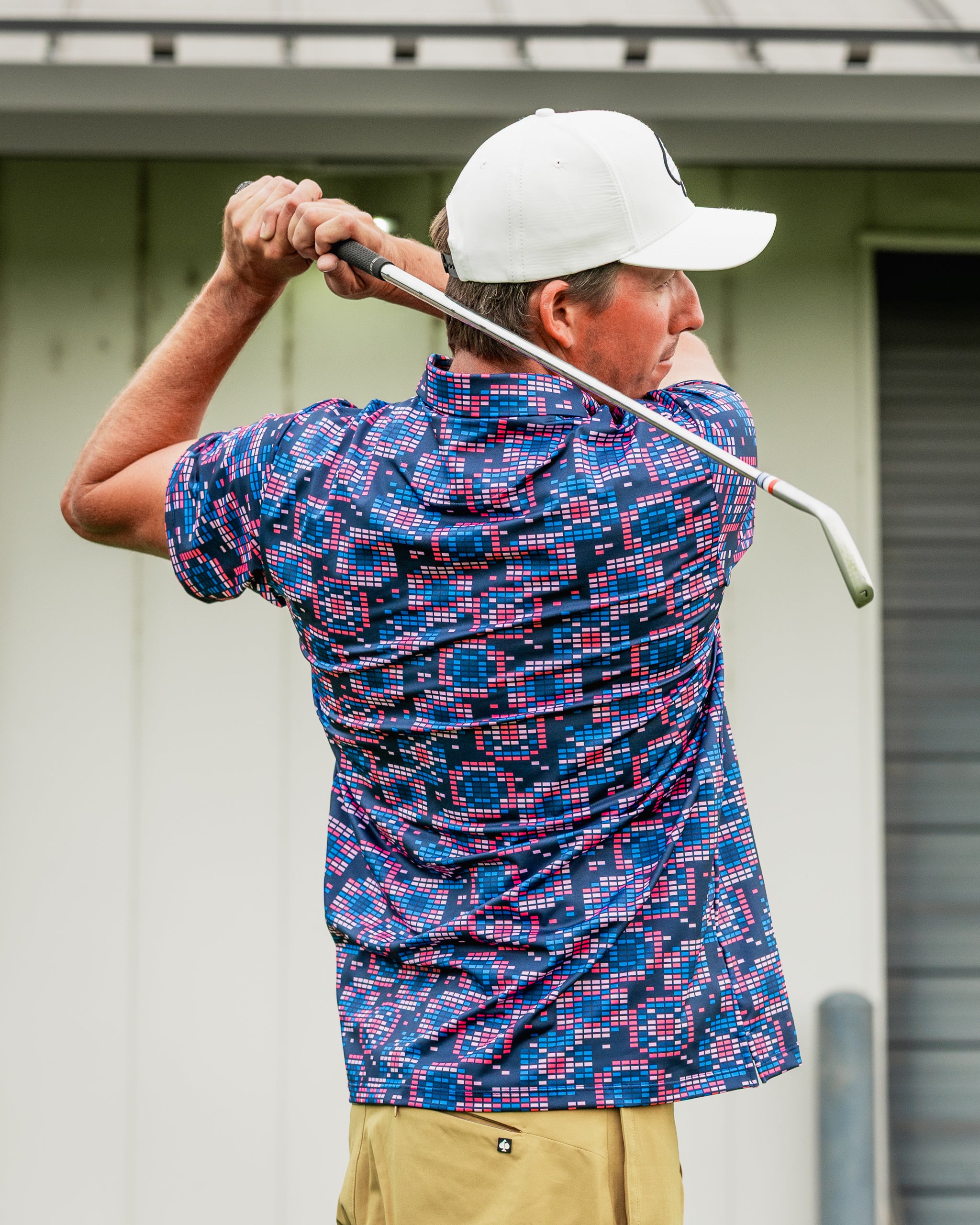 Golfer in a Tetrafloral Dark shirt with a colorful geometric pattern, preparing to swing a golf club on the course.