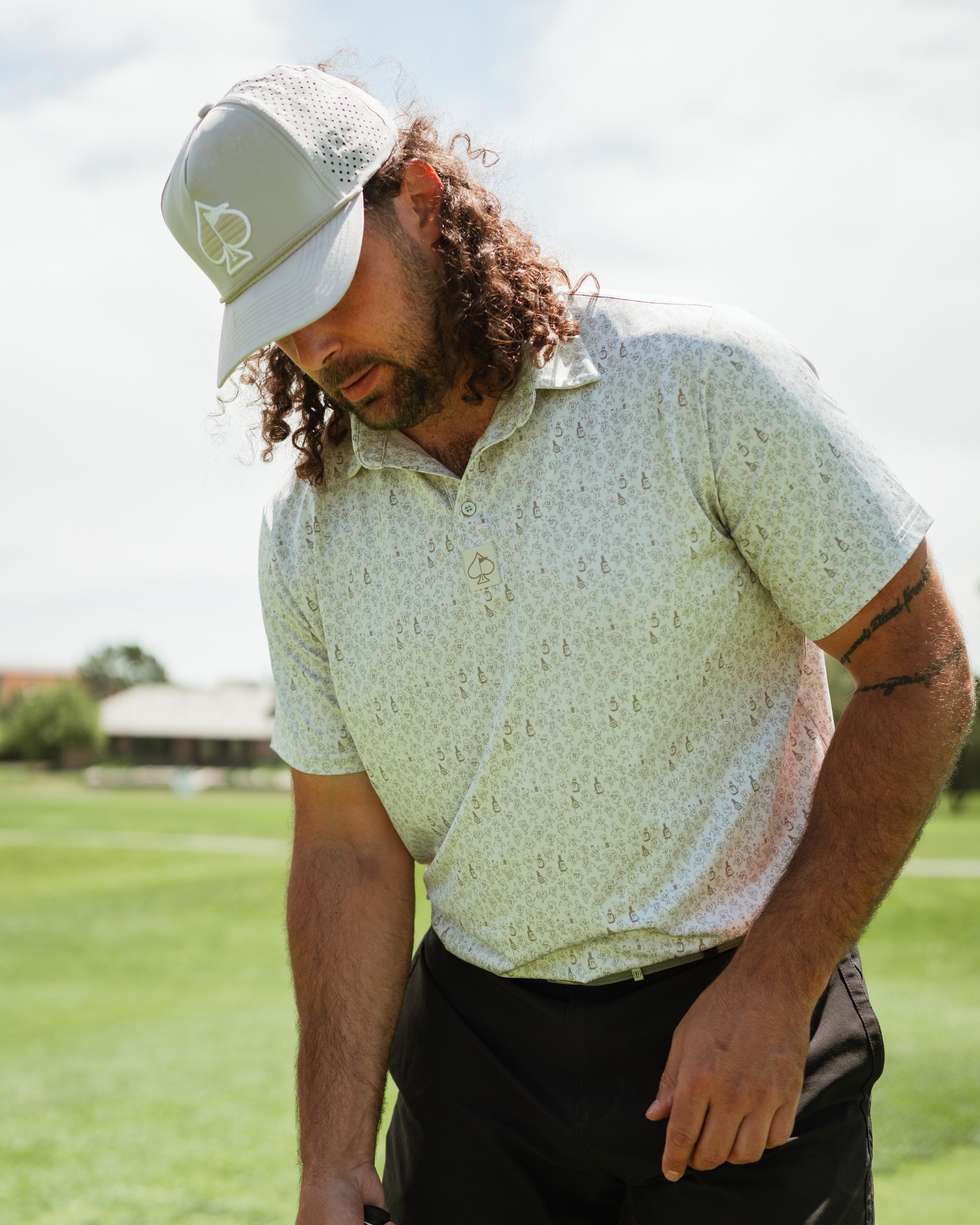 Man wearing a light-patterned polo shirt and a gray cap, focusing on his golf swing on a sunny course.