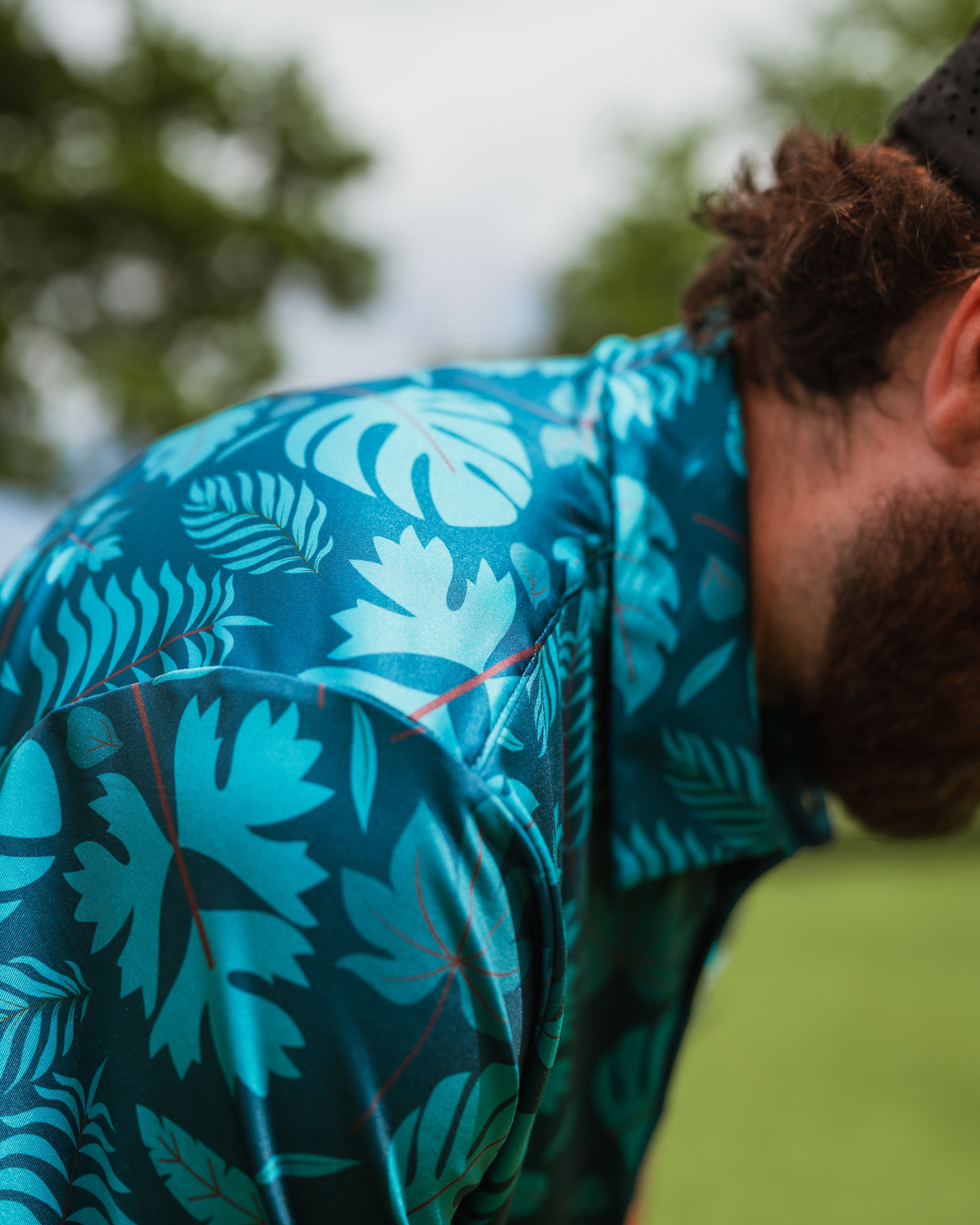 Bold tropical print golf shirt featuring vibrant blue and green foliage, perfect for stylish summer play on the course.