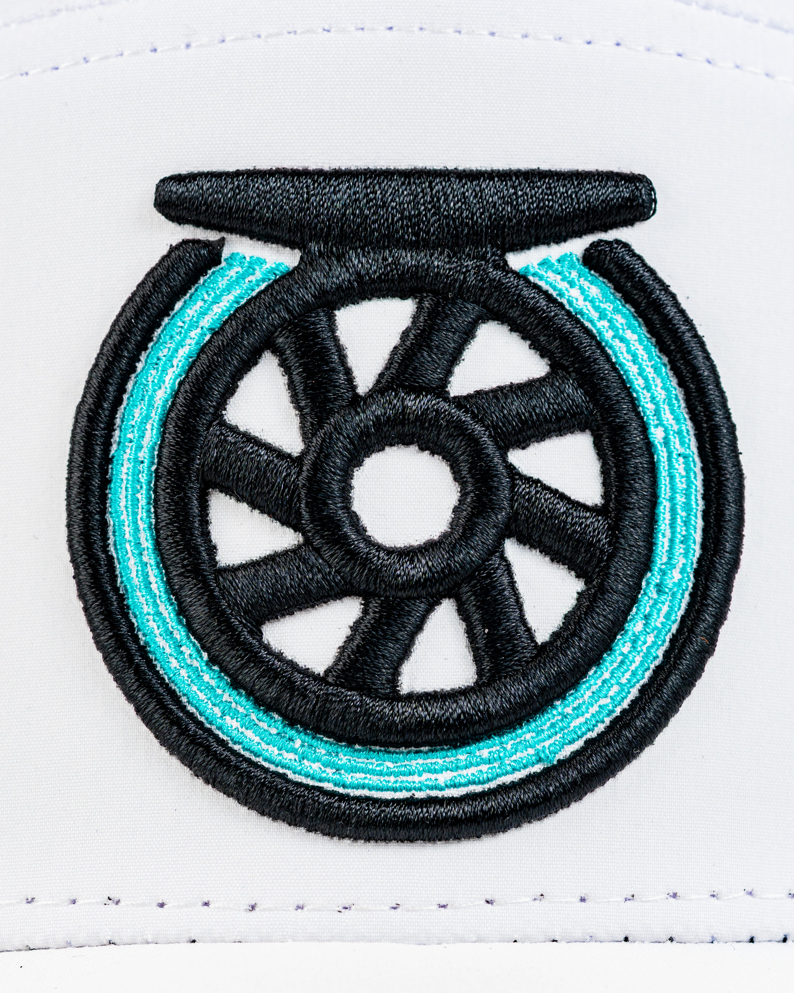 Close-up of the Tradesman Hat featuring a bold embroidered wheel design in black and teal on a white background.