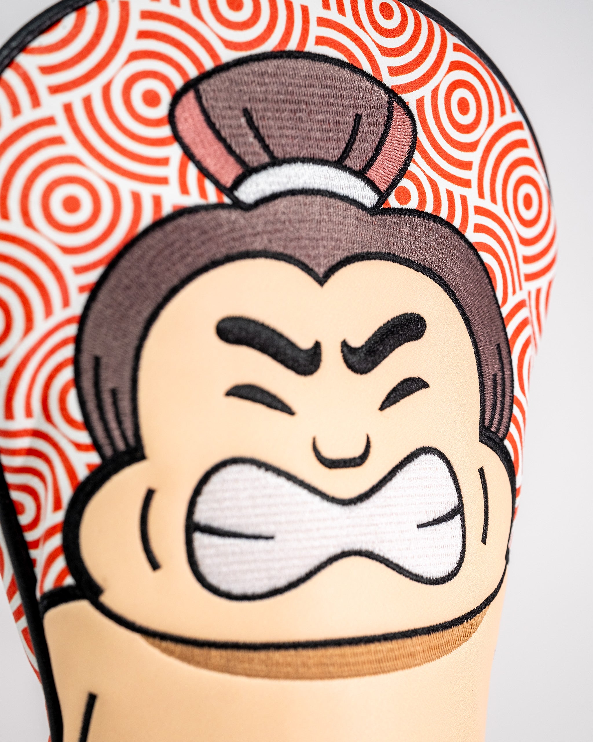 Close-up of a golf driver cover featuring a cartoon character with an angry expression, bold eyebrows, and a patterned background.
