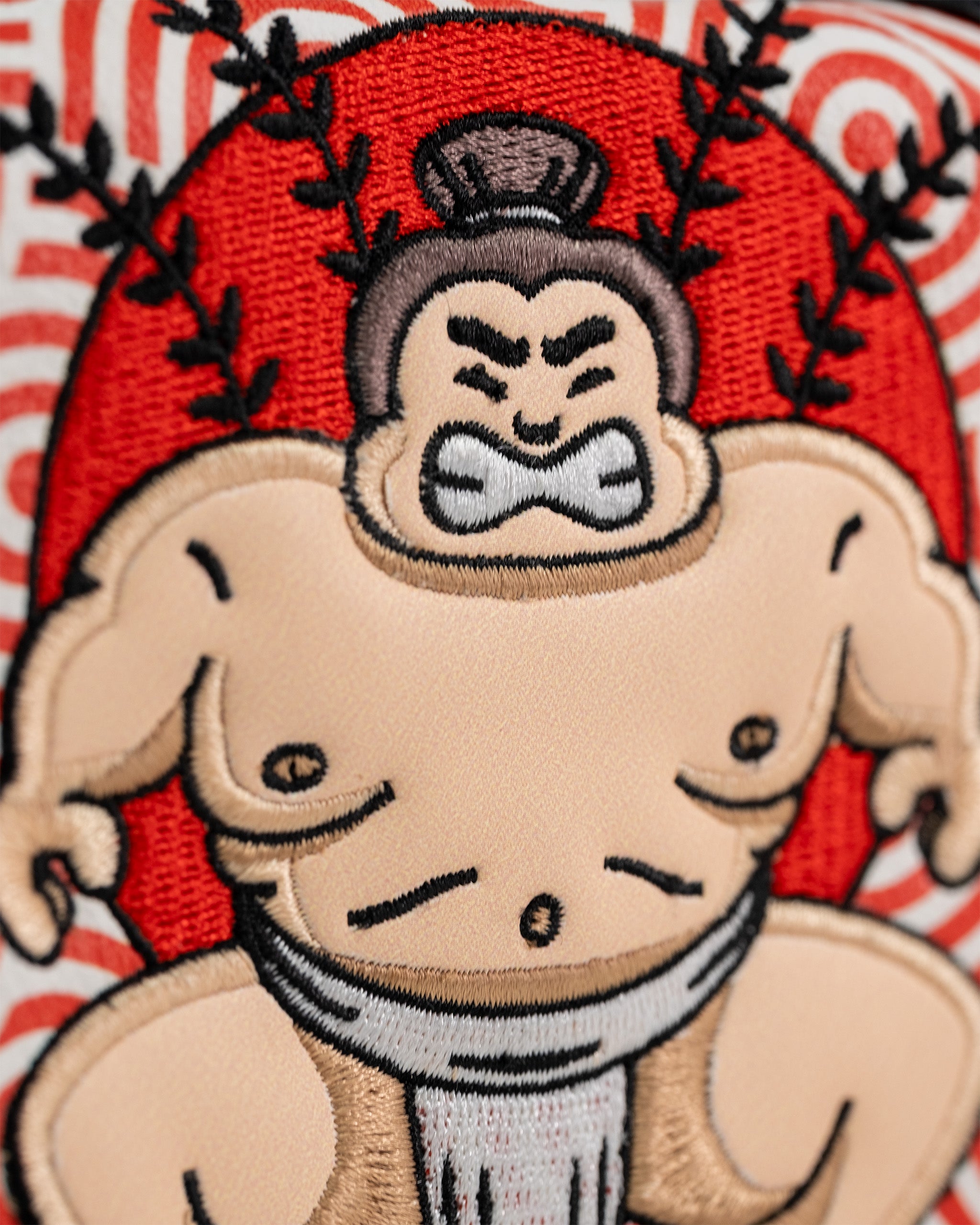 Embroidered patch of a sumo wrestler with a fierce expression, red background, and detailed stitching on a golf club mallet cover.