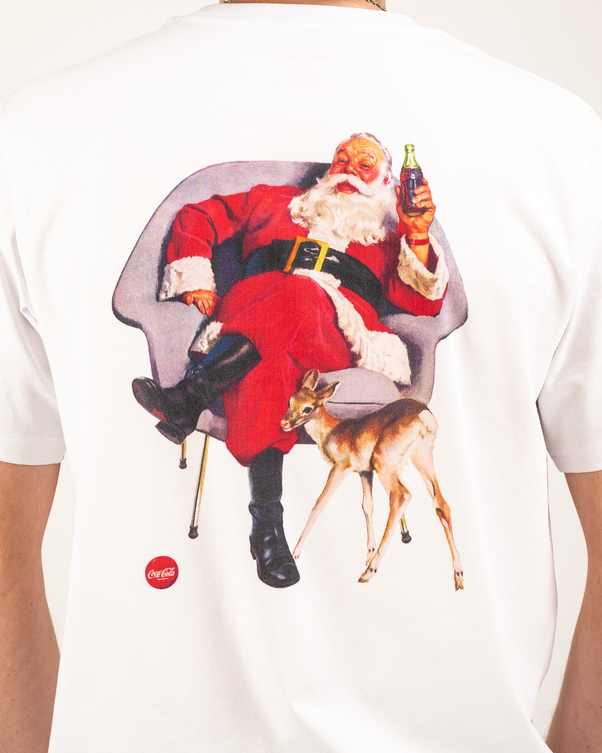 Vintage Coca-Cola tee featuring Santa Claus relaxing in a chair with a deer, capturing a festive holiday spirit.