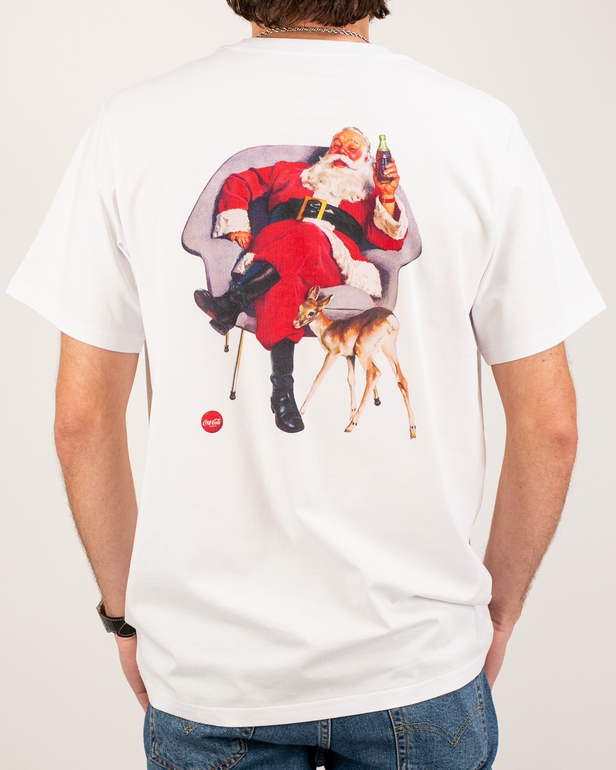 White tee shirt featuring a vintage Santa Claus relaxing in a chair with a reindeer at his feet, holding a Coca-Cola bottle.