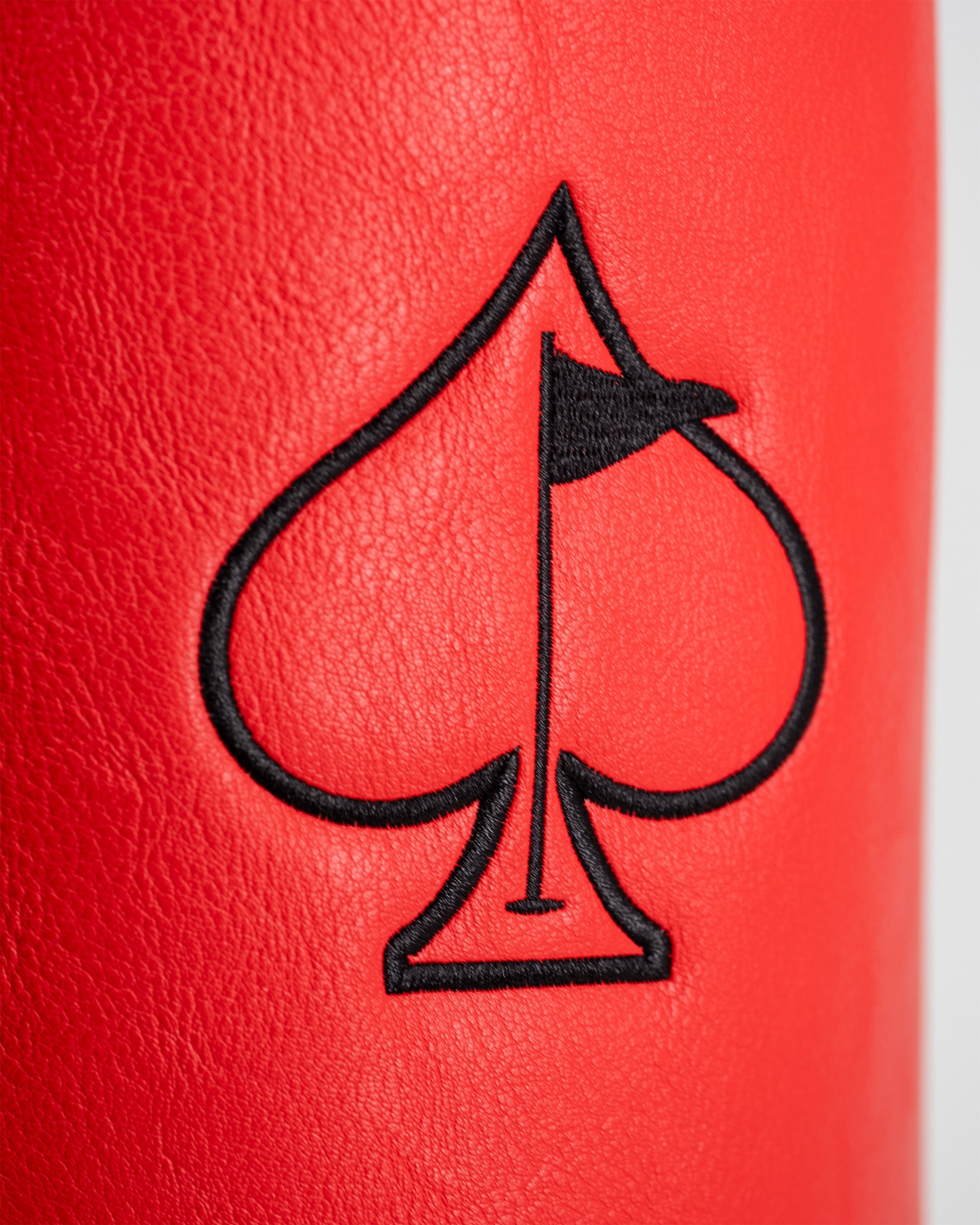 Close-up of a red golf driver cover featuring a black embroidered spade symbol with a small flag at the top.