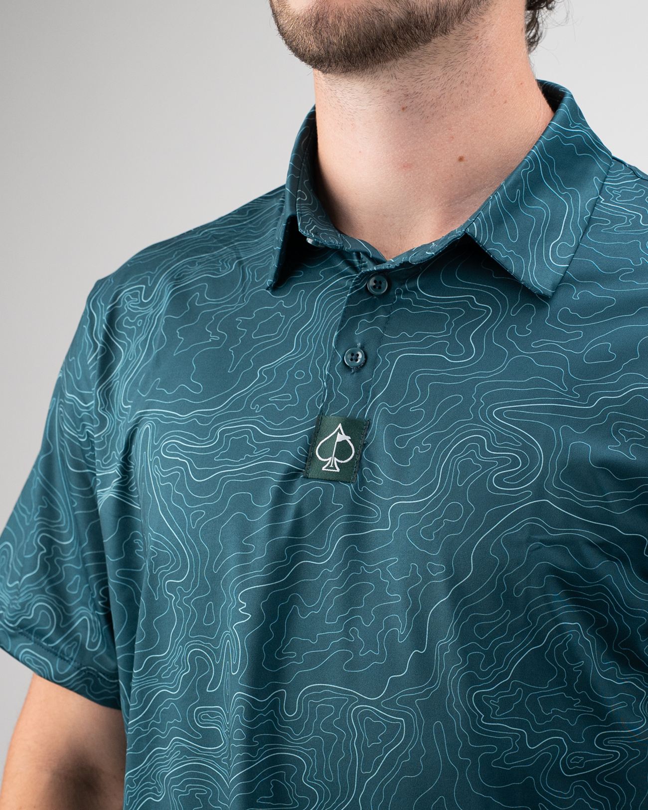 Men's Terrain golf polo featuring a topographic design in teal, with a subtle logo on the collar. Perfect for stylish golfers.