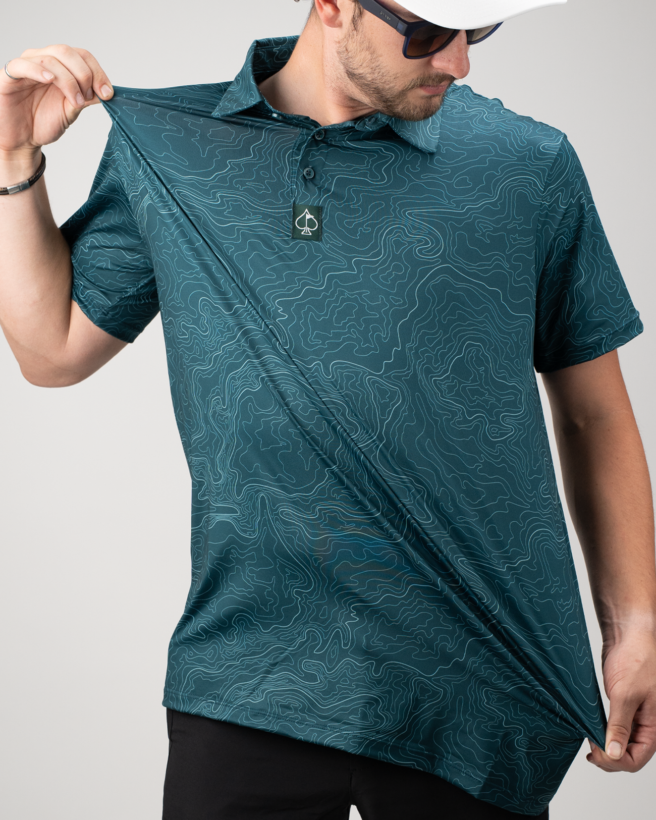 Man showcasing a teal Terrain polo shirt with a topographic pattern, highlighting its lightweight and stylish design.