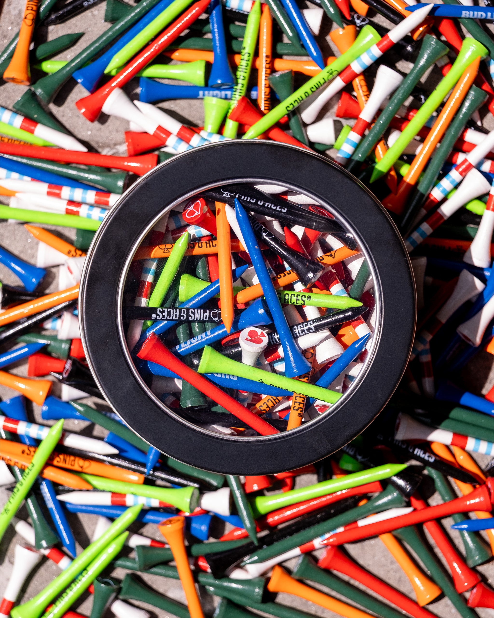 A tin labeled "Tin of Tees" filled with colorful golf tees, surrounded by more golf tees scattered on a surface.