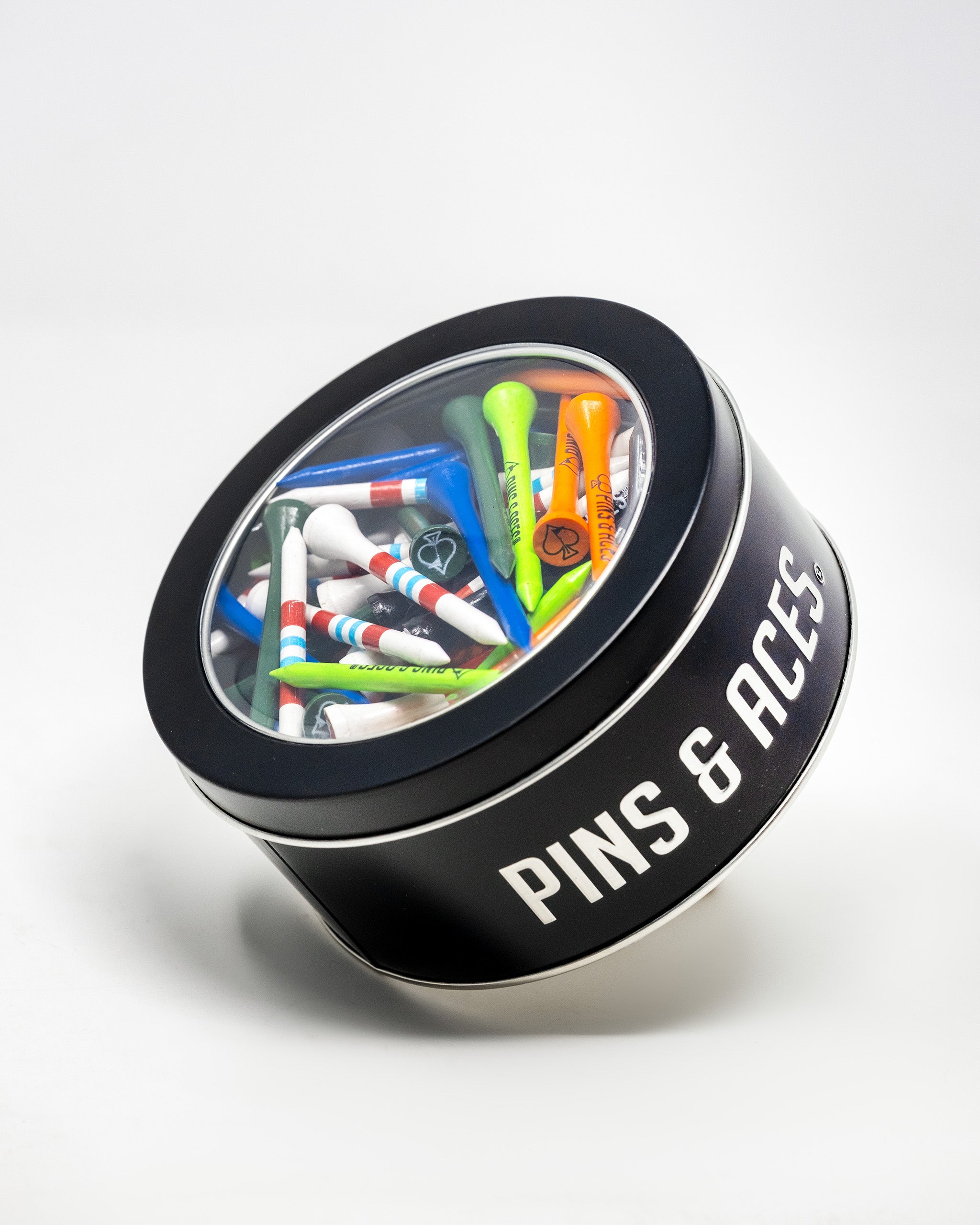 A round black tin labeled "PINS & ACCESSORIES" with a clear lid, filled with colorful golf tees inside.