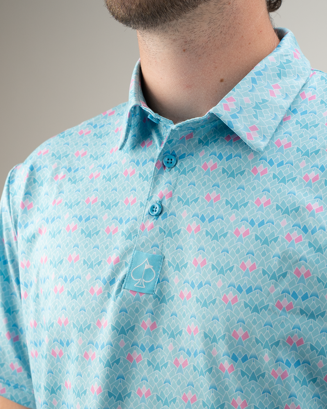 Men's golf polo shirt featuring a blue triangle bloom pattern with pink accents and a small embroidered logo on the chest.