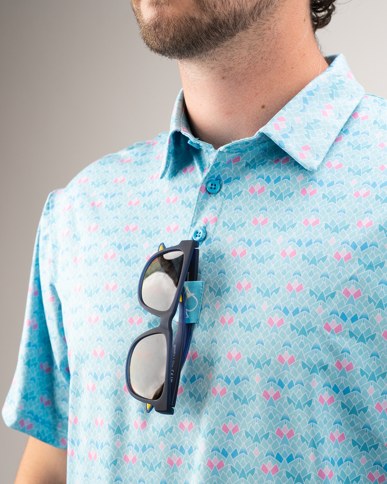 Man wearing a light blue polo shirt with a pink triangle pattern, sunglasses resting on the collar.