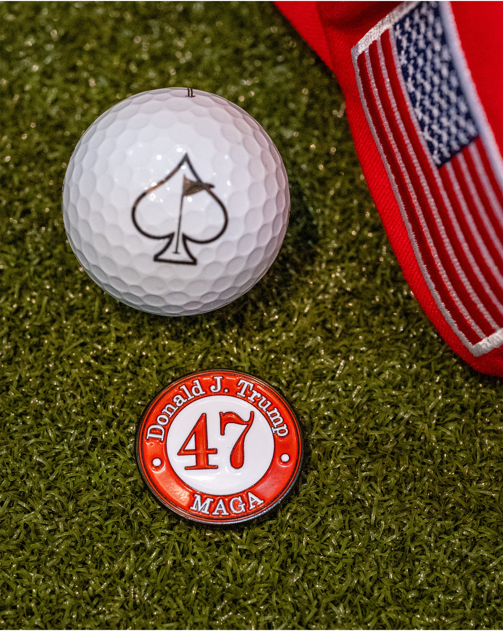 "47 Ball Marker featuring Donald J. Trump and MAGA, placed on green turf with a golf ball and red cap.