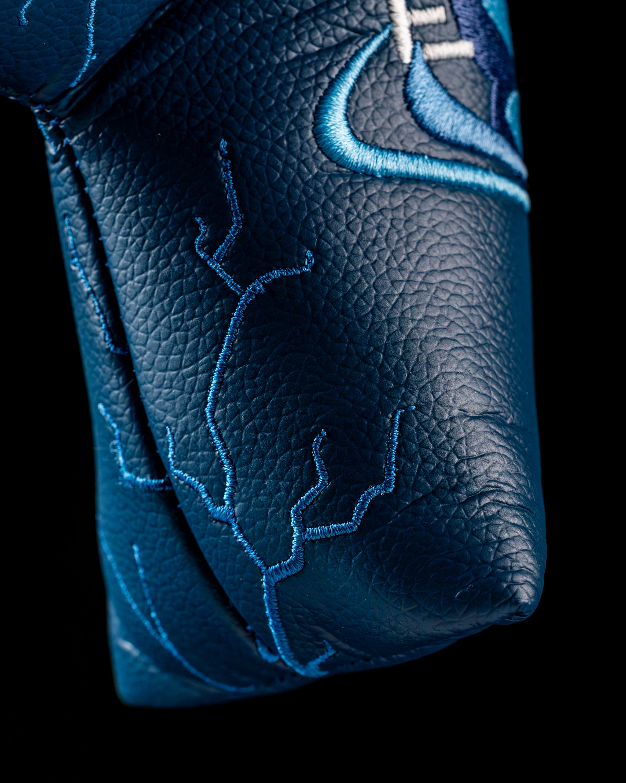 Close-up of the Edel Twister Putter headcover featuring intricate blue stitching on a textured leather background.