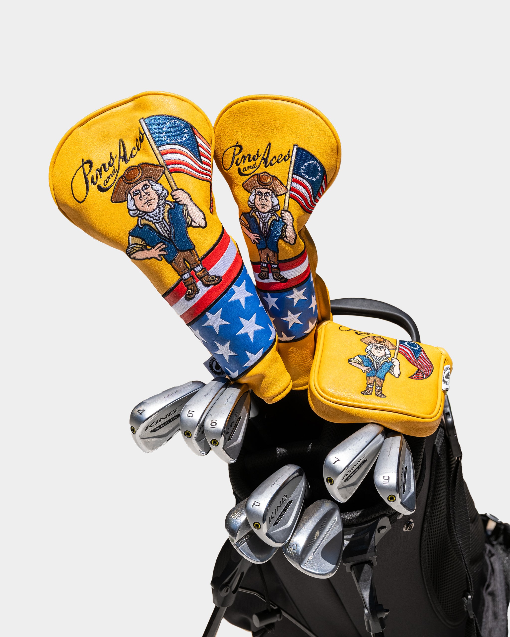 Bright yellow golf headcovers and accessories featuring patriotic cartoon character with an American flag, stars, and bold...