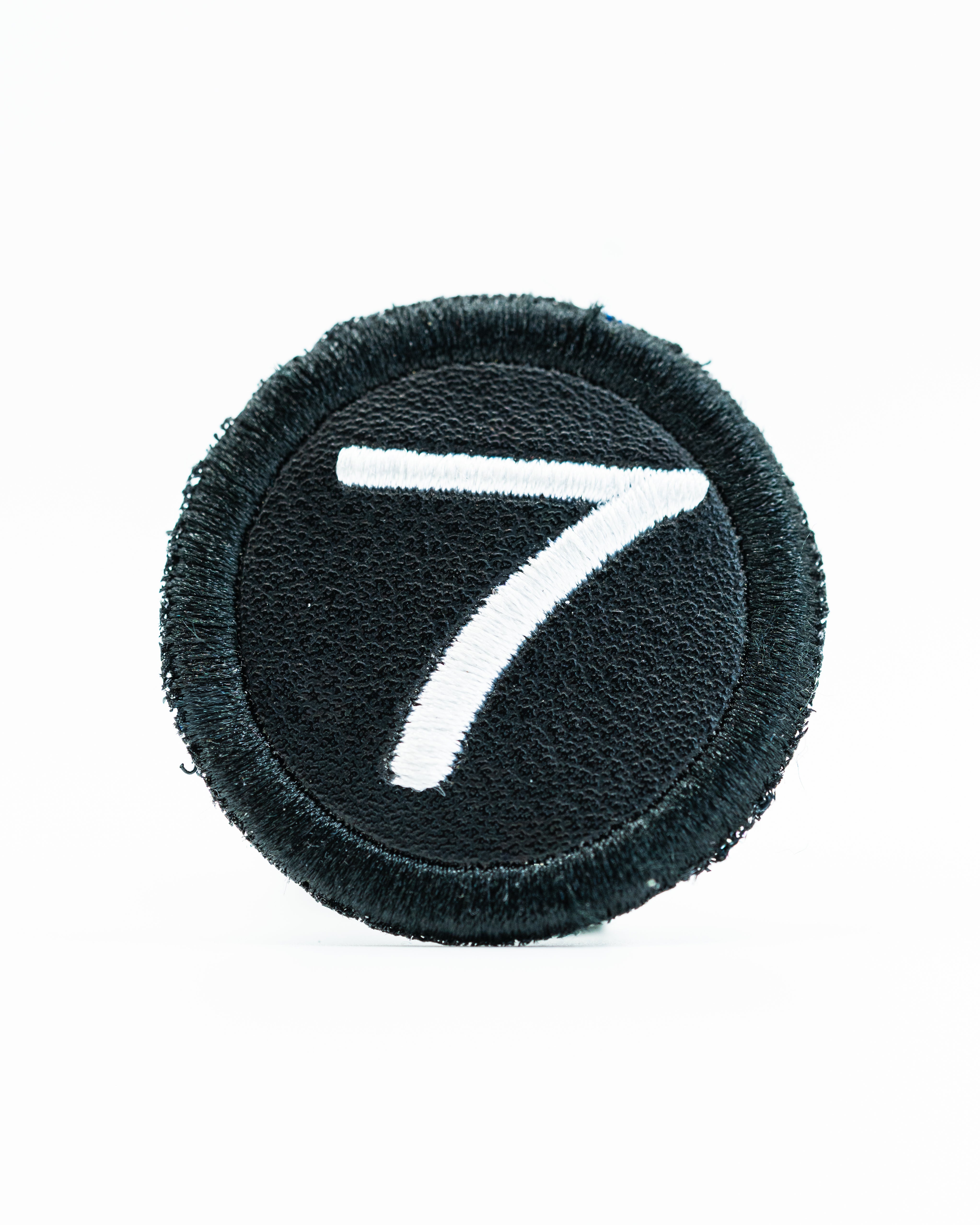 Black headcover patch featuring a white embroidered number seven, designed for golfers to personalize their gear.