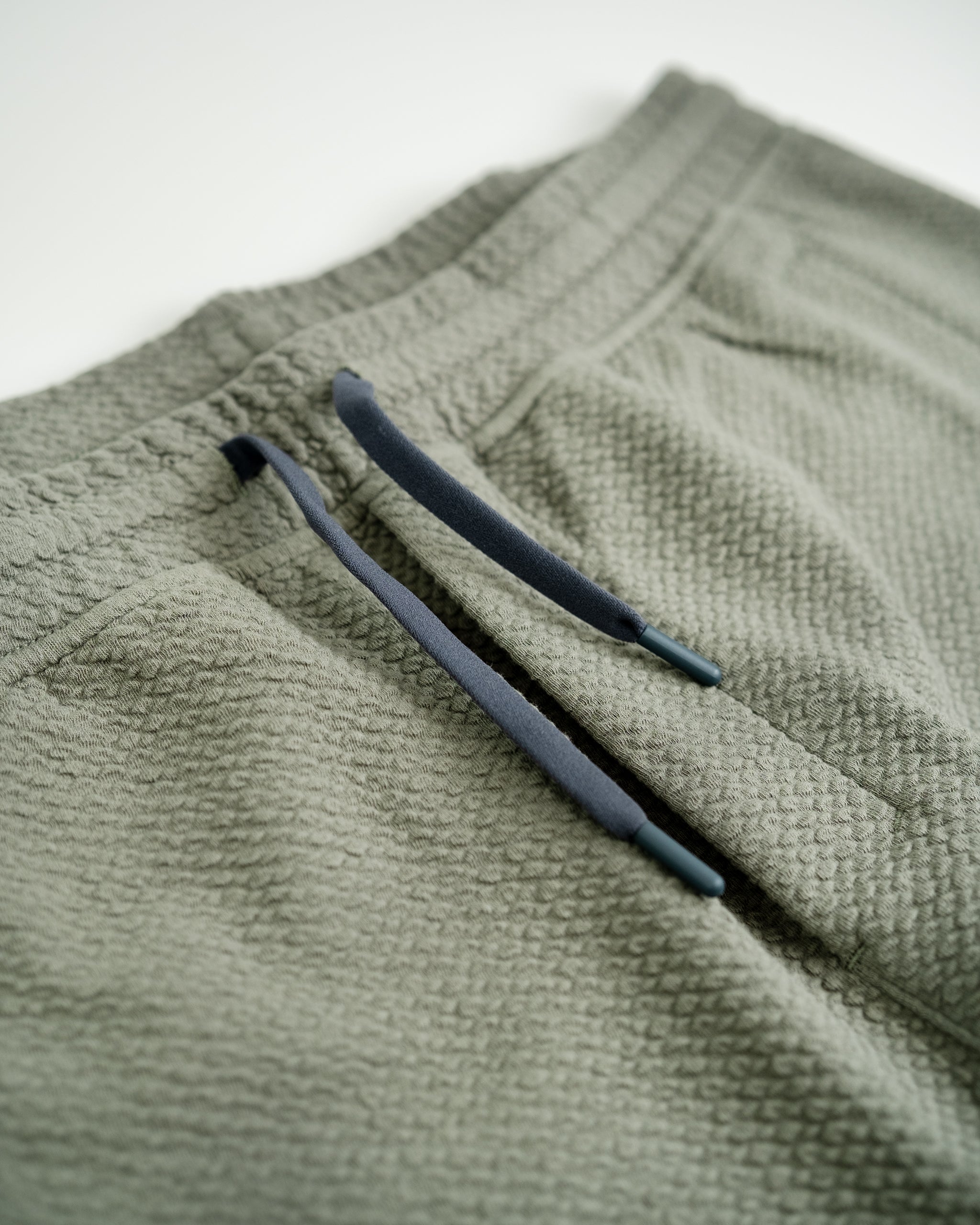 Close-up of olive green textured golf joggers with dark navy drawstrings, showcasing bold, unique style for golfers.