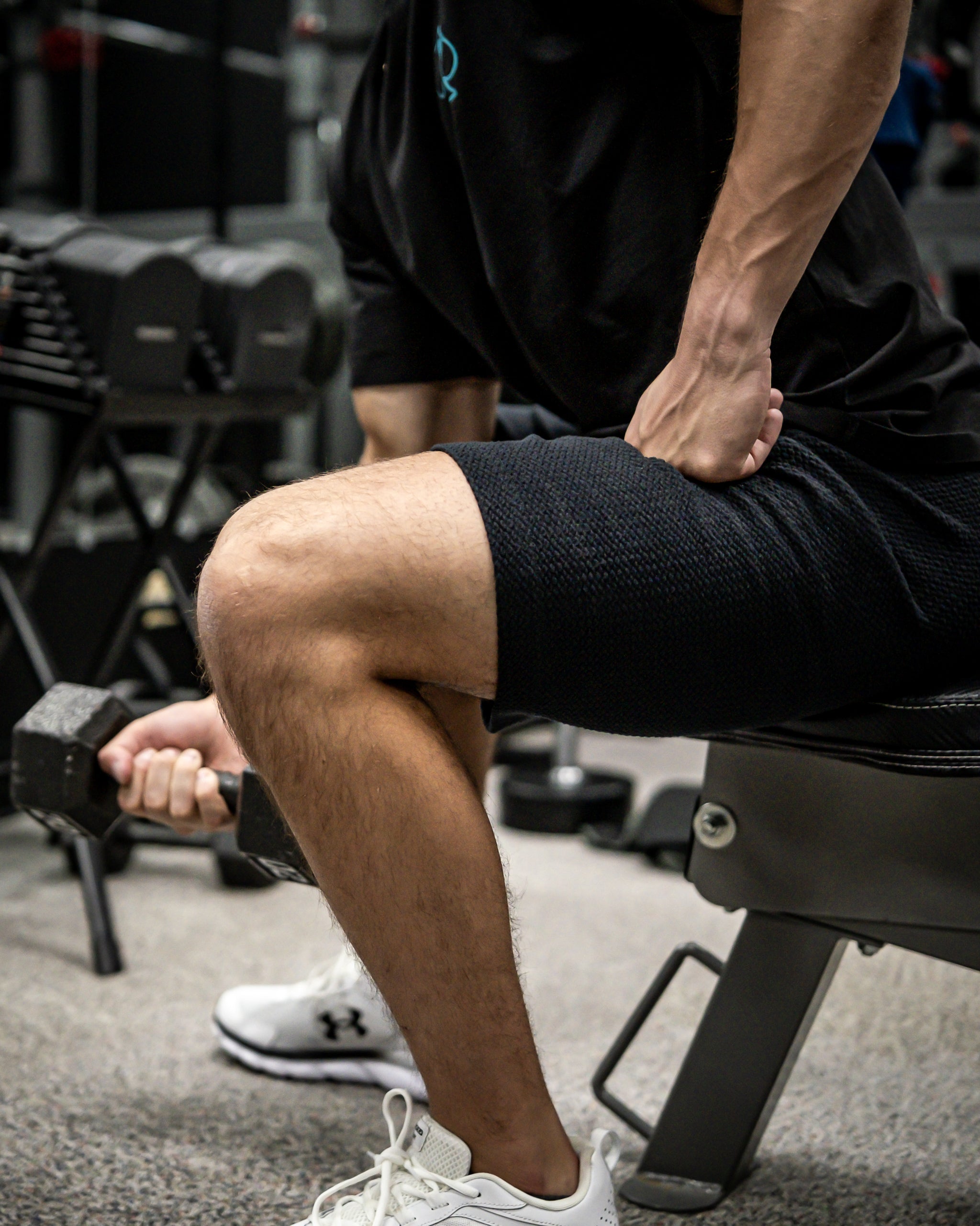 Close-up of a man in black athletic wear performing a seated dumbbell curl, highlighting muscular arms and textured black ...
