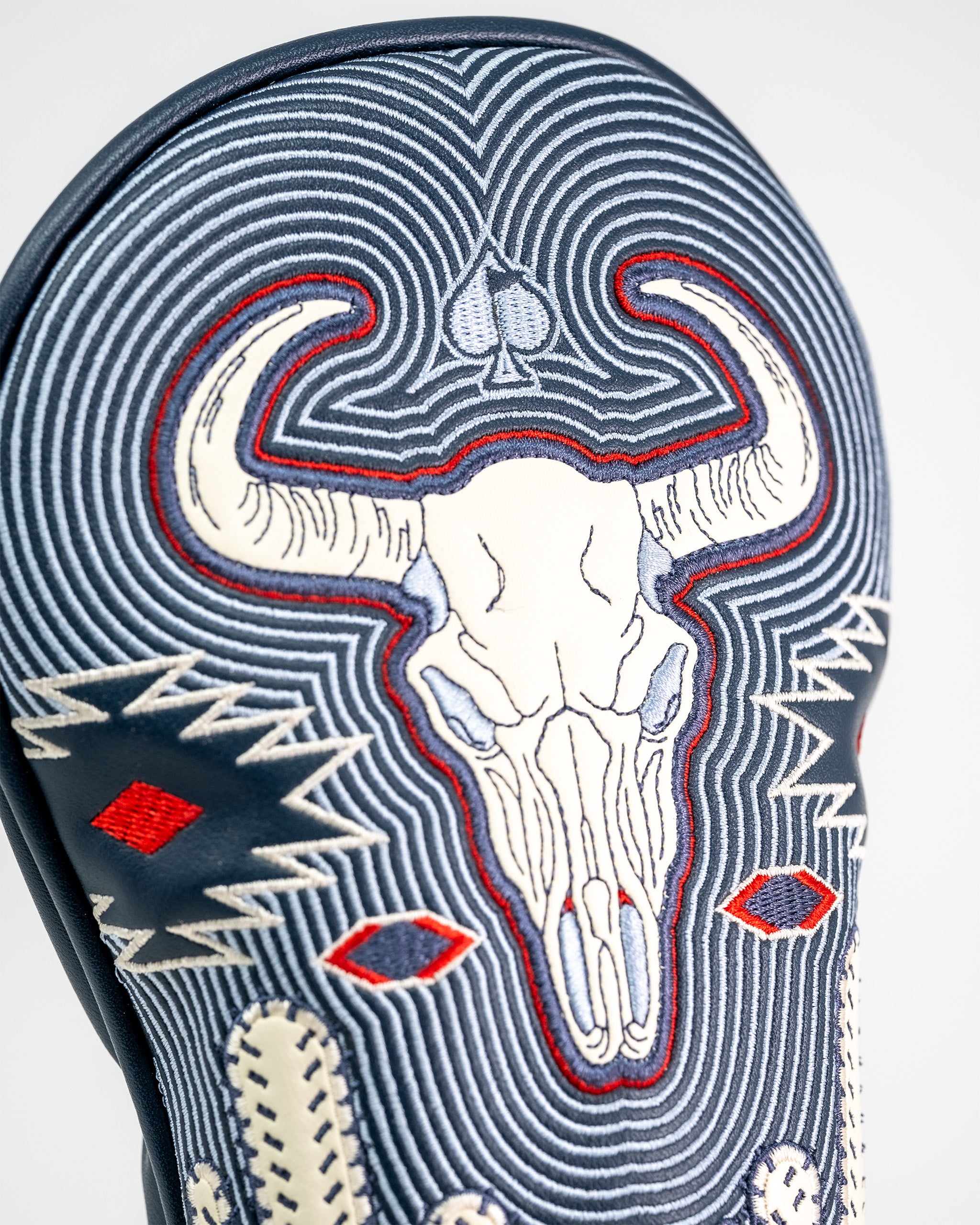 Embroidery of a skull with horns and a spade symbol on a navy blue fairway golf club cover with intricate stitching and western design.