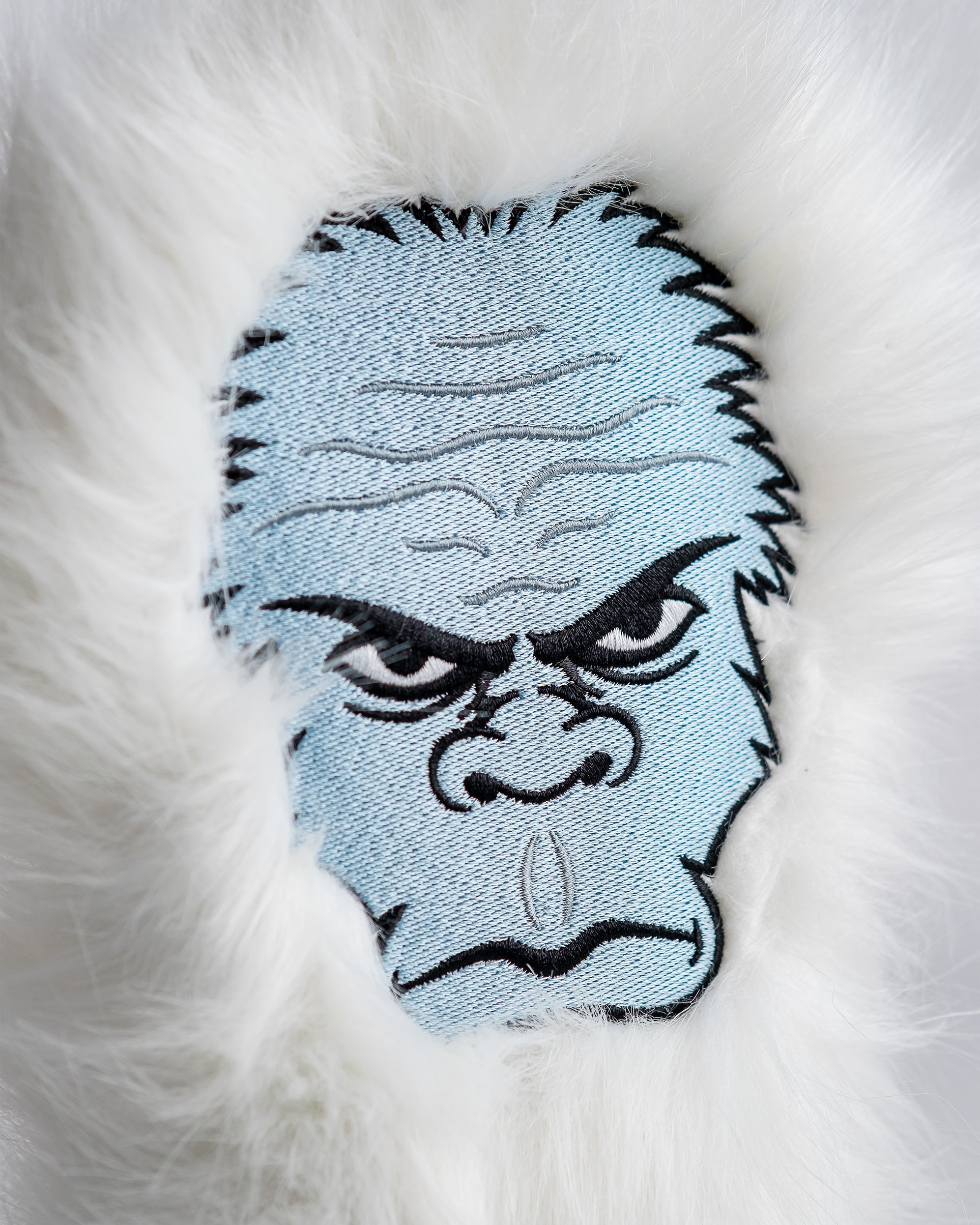 Close-up of a white faux fur golf club headcover with an embroidered fierce face design, featuring intense eyes and bold d...
