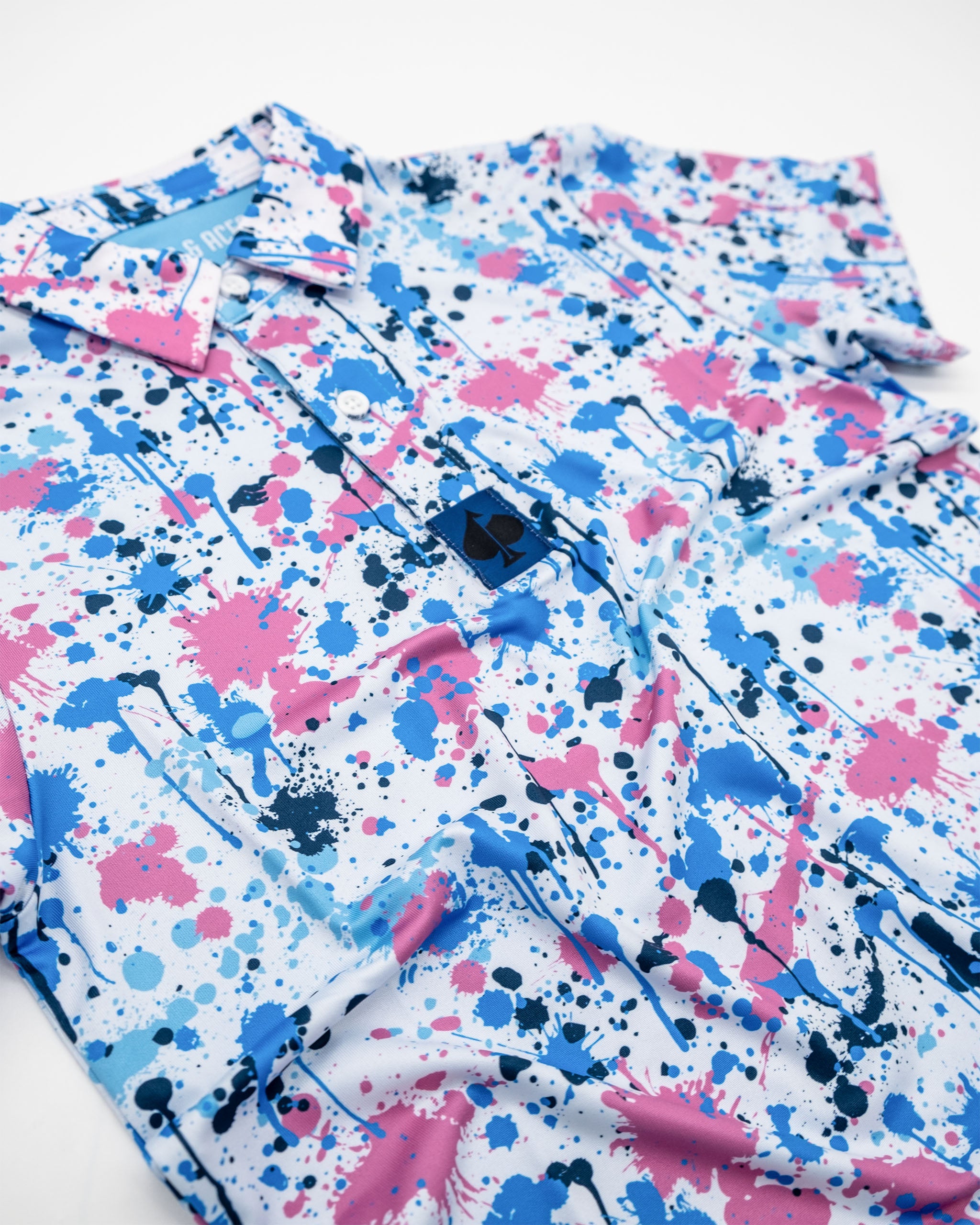 Youth Cotton Candy Drip Polo featuring a vibrant splatter design in pink, blue, and black on a white background.