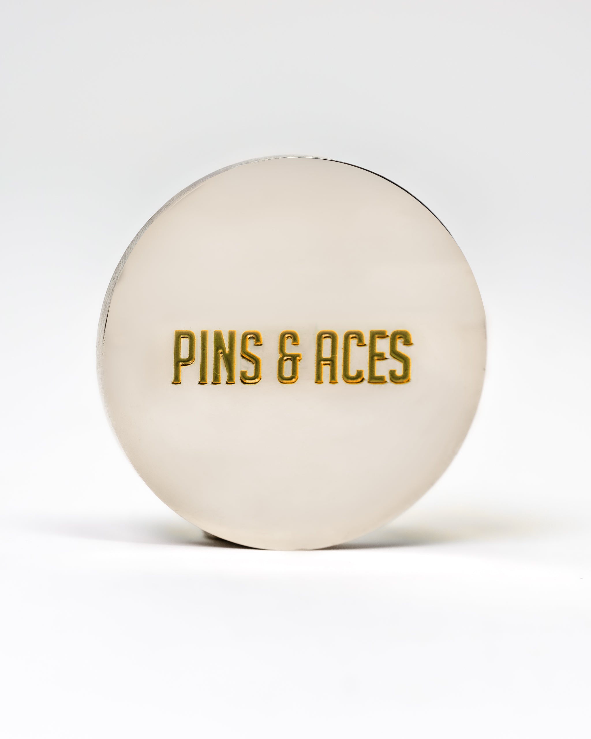 "6 Milly Cinnamon Ball Marker featuring 'PINS & ACES' engraved in gold on a silver circular surface.
