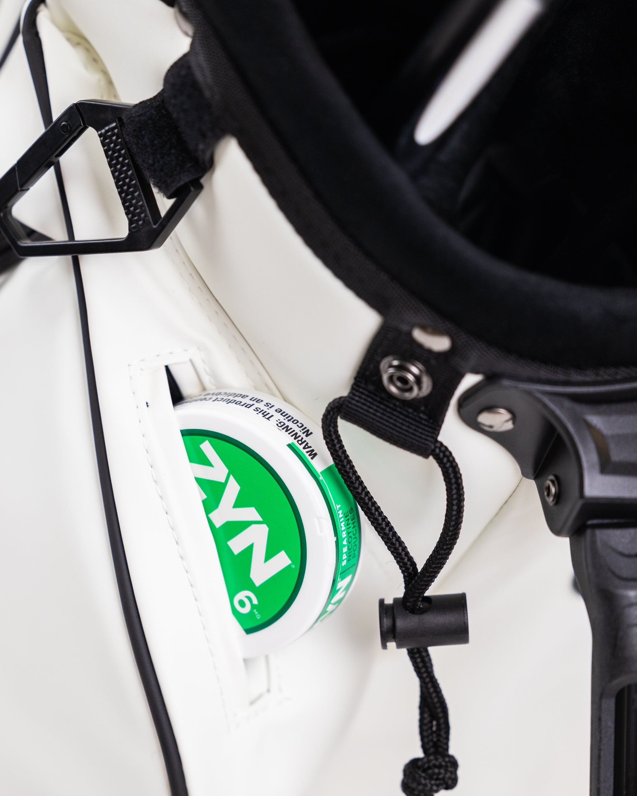 Close-up of a white golf cart with a green and white NYN logo sticker, black strap, and black accessories for bold golf st...