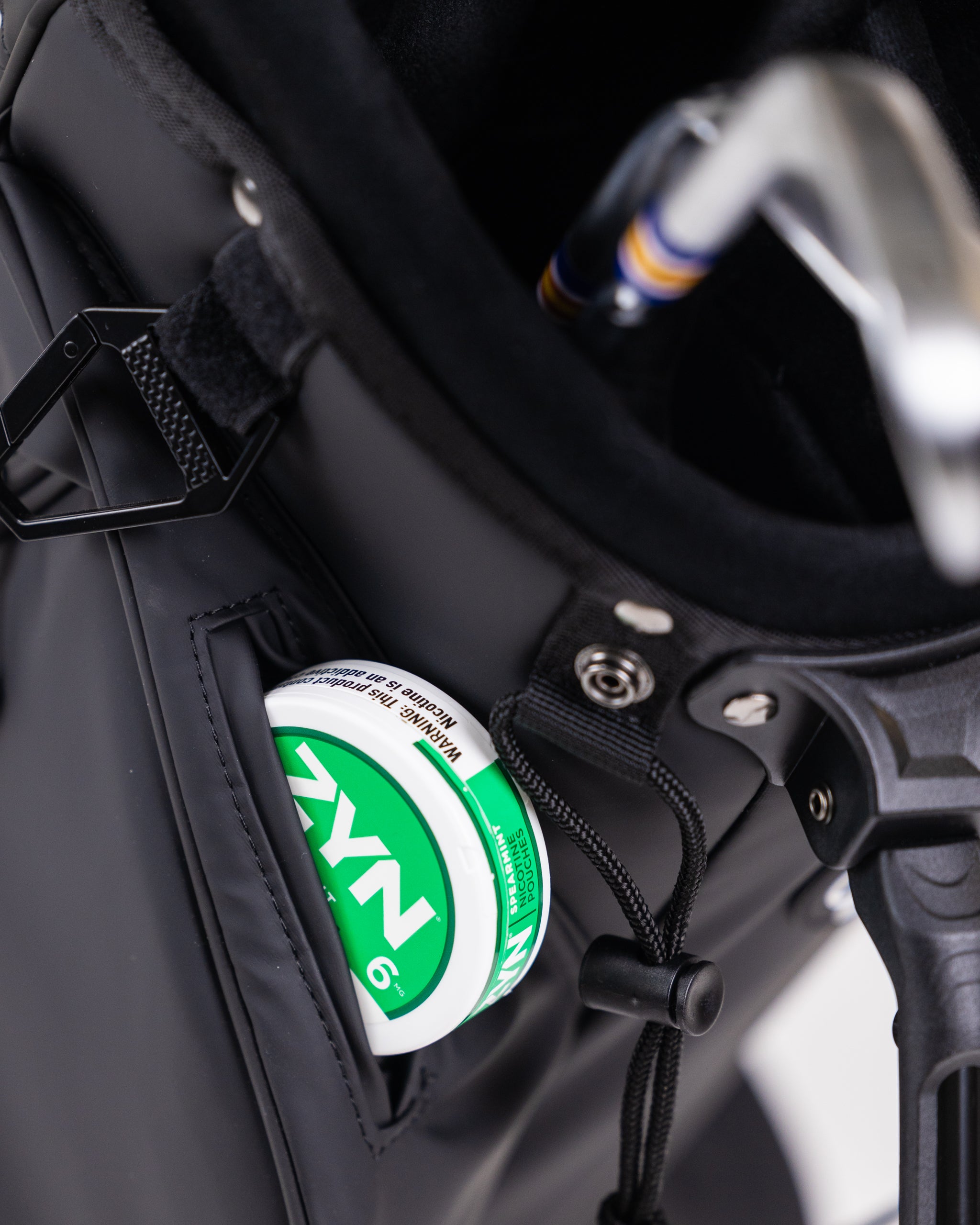 Close-up of a black golf cart with a green and white WAGNER golf accessory tucked in a pocket, featuring bold colors and s...