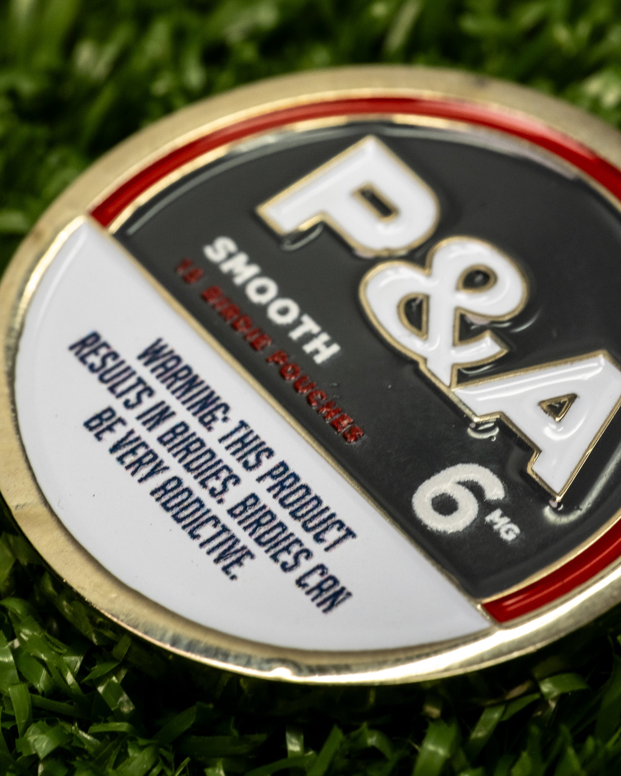 Close-up of a 6 Milly smooth ball marker featuring a warning about its addictive nature for birdies.