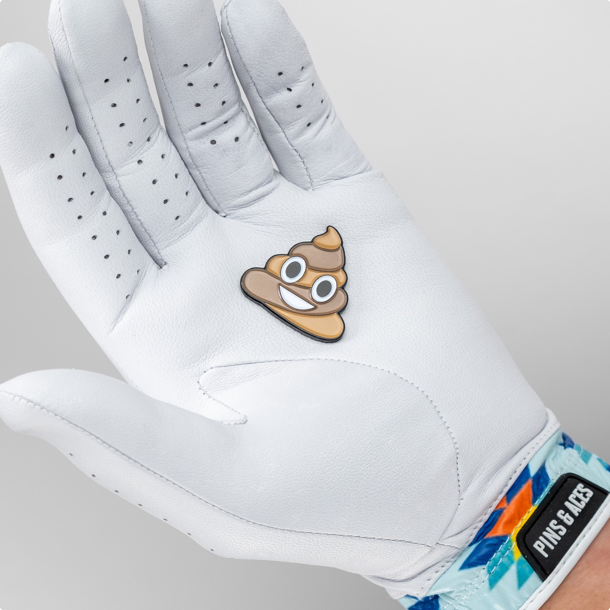 A novelty poop ball marker designed for golfers, featuring a playful cartoonish poop emoji with a smiling face, set against a black background.