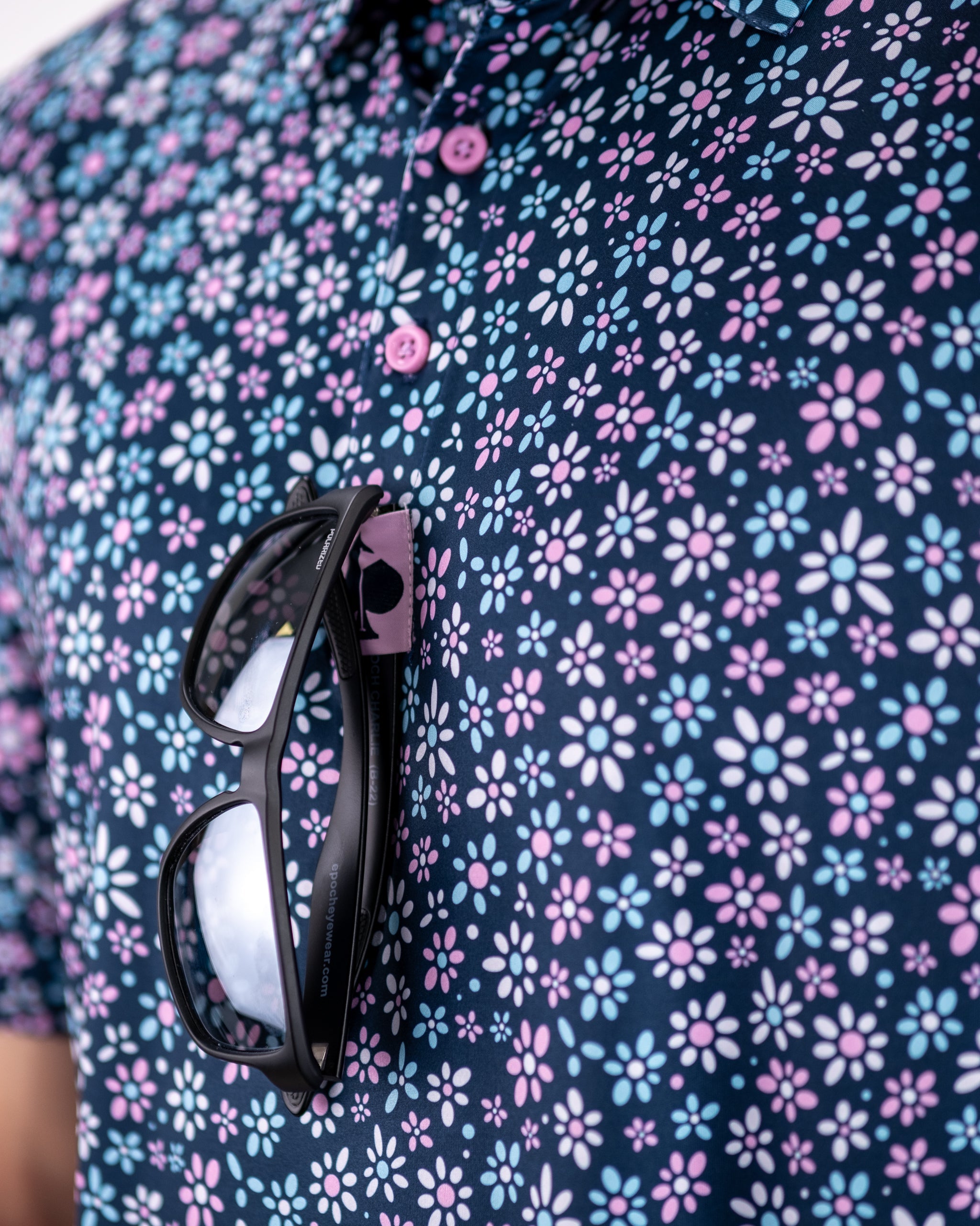 Bold navy polo shirt with a vibrant floral pattern in pink and blue, featuring sunglasses tucked into the collar.