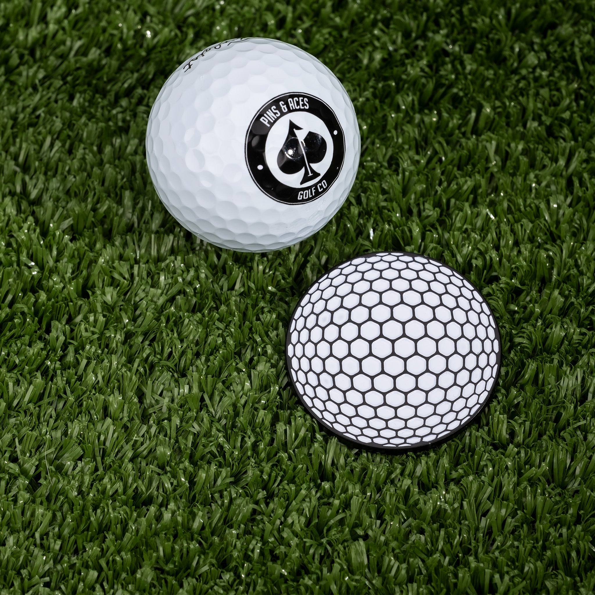 Golf ball marker featuring a honeycomb design next to a golf ball with a logo, set on green turf.