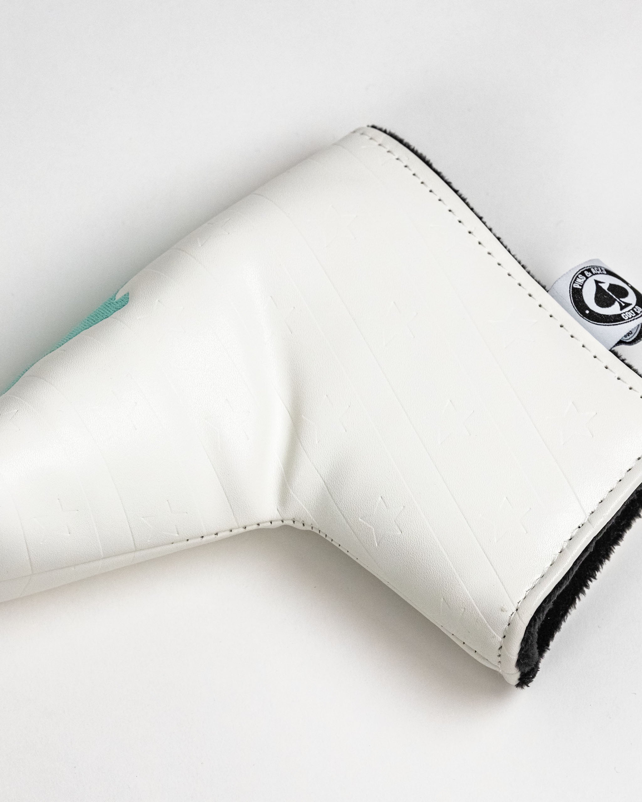 White blade putter cover with embossed star pattern and a teal logo, designed for golfers seeking a stylish accessory.