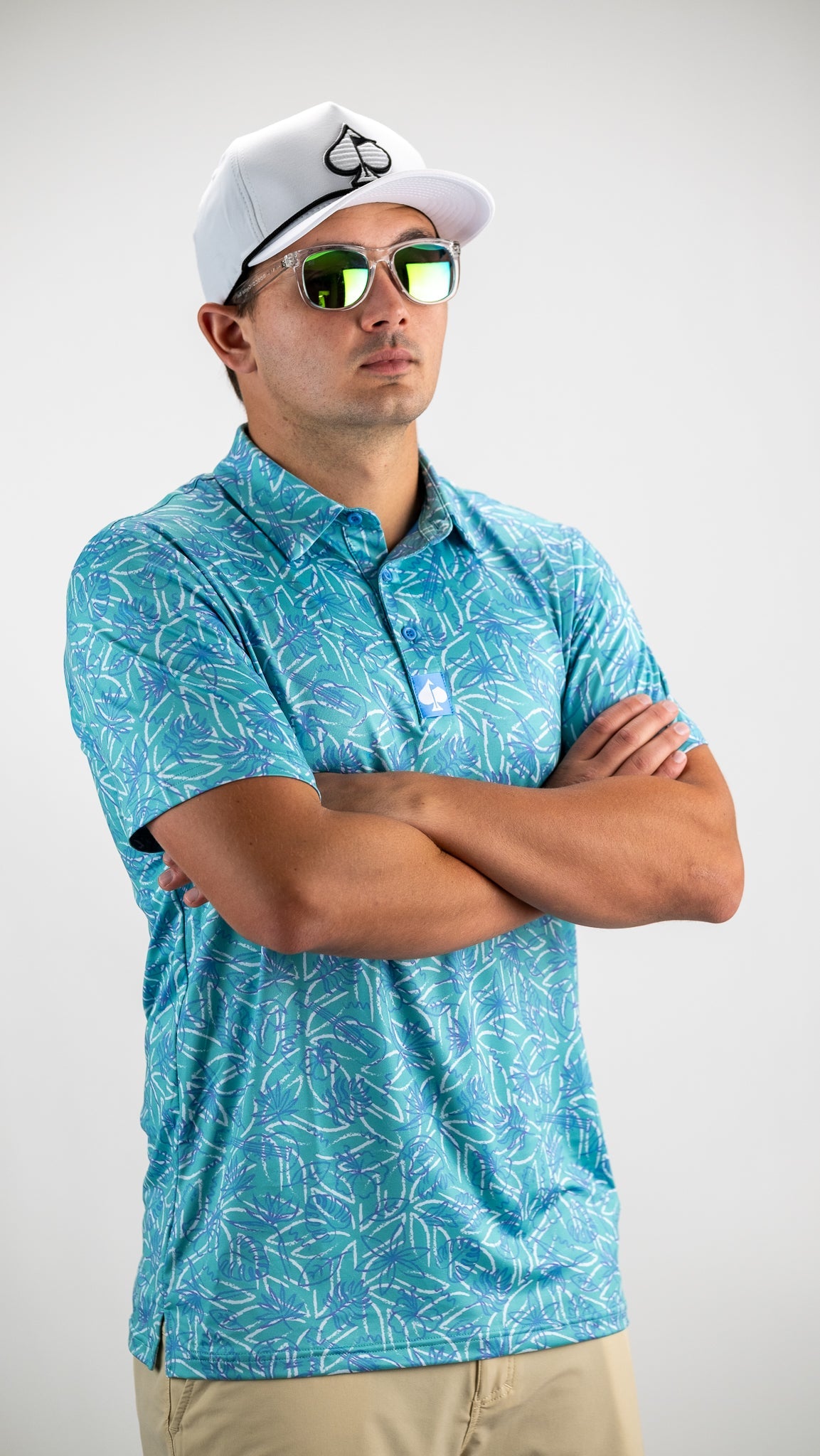 Model wearing a Margaritaville 5 O'Clock Ocean golf shirt featuring a vibrant tropical pattern, paired with stylish sunglasses and a cap.