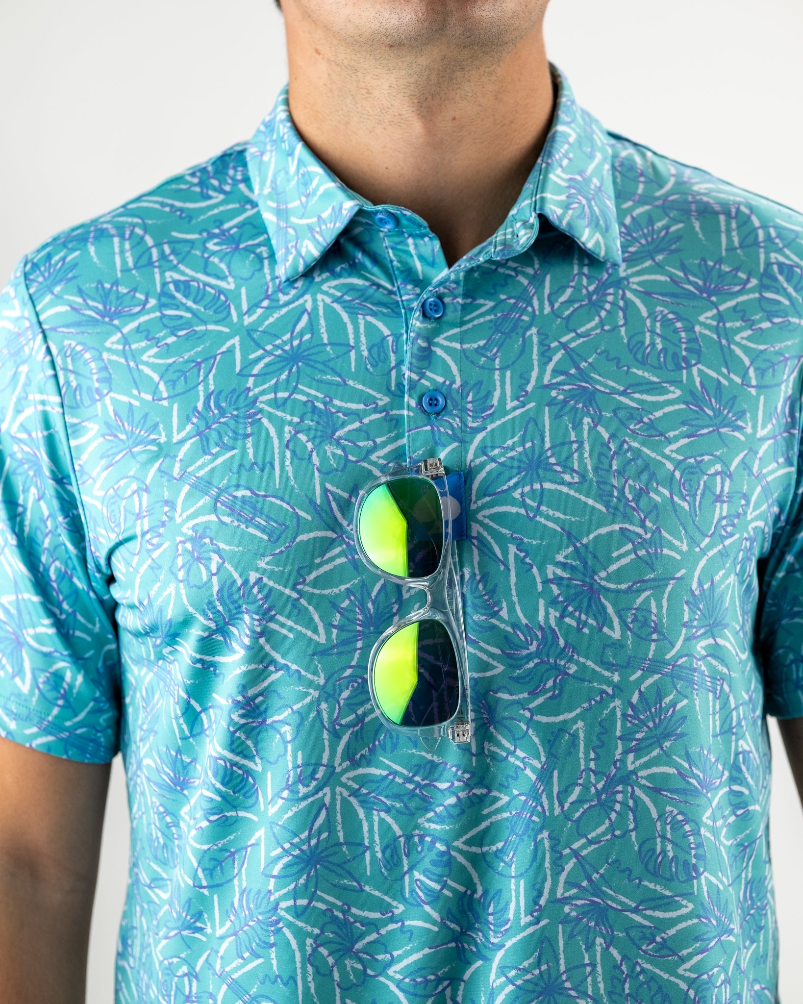 Men's Margaritaville 5 O'Clock Ocean golf shirt featuring a vibrant tropical pattern, with sunglasses hanging from the collar.