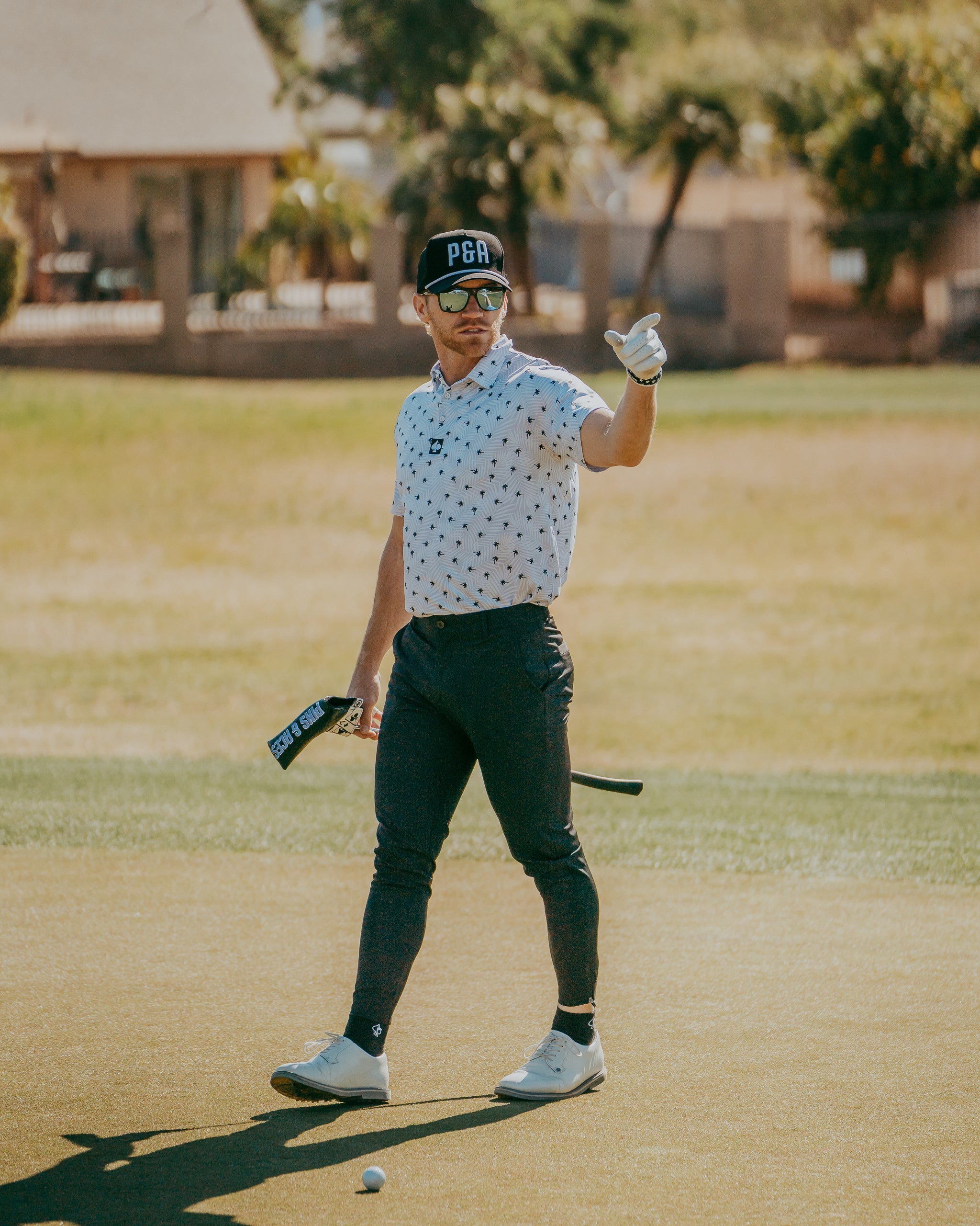 A golfer in a patterned polo shirt and stylish cap gestures confidently on the course, showcasing bold golf fashion.