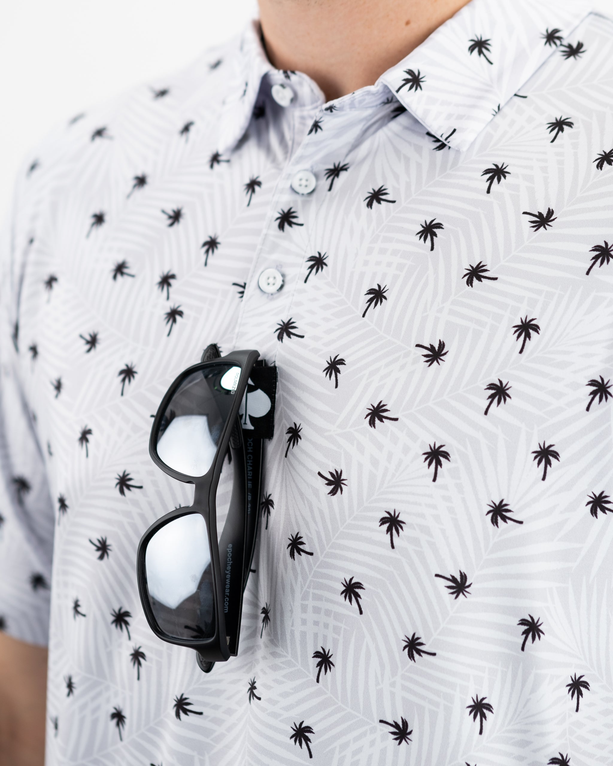 Men's golf polo shirt featuring a stylish palm tree pattern, paired with sunglasses resting on the collar.