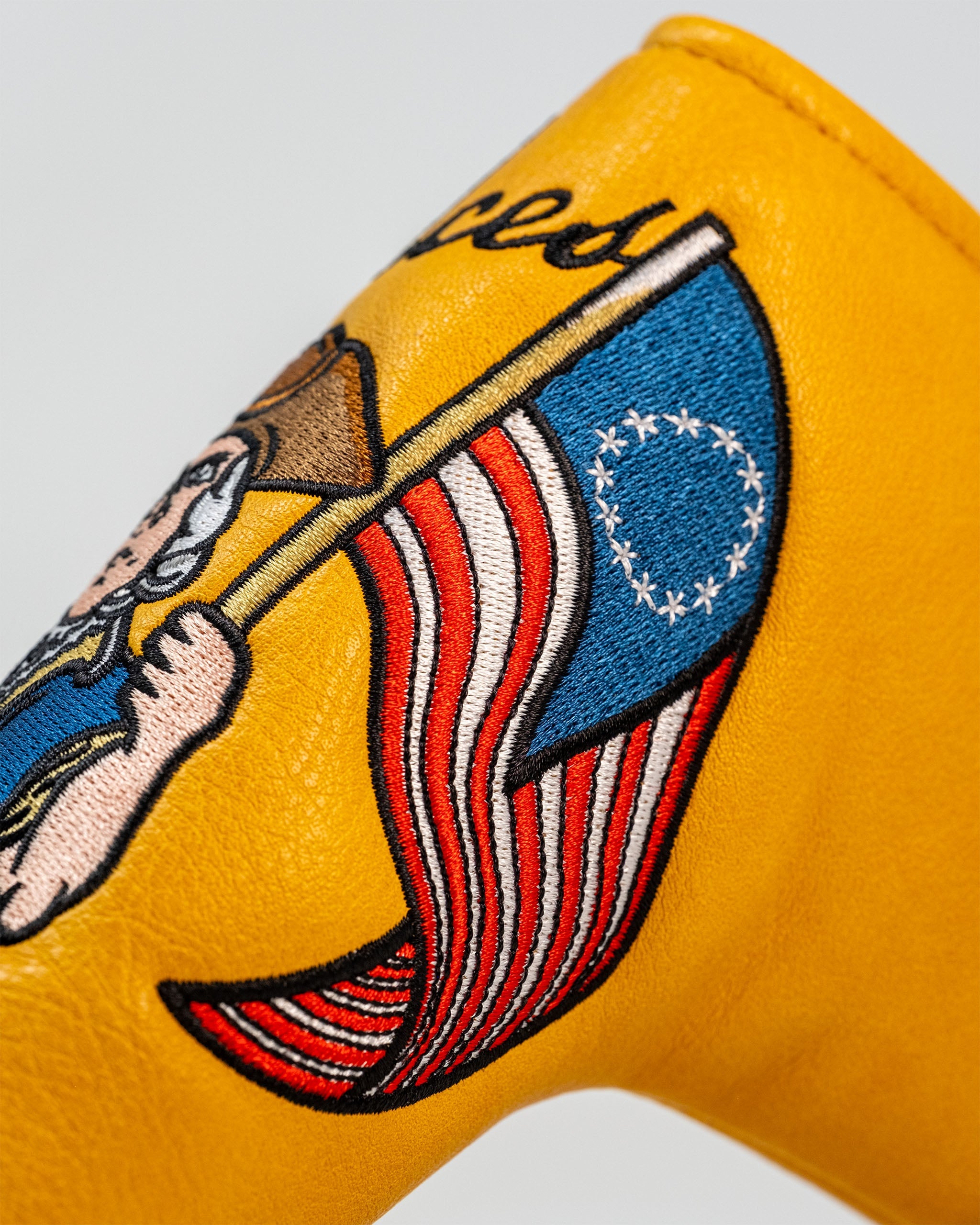Patriot Blade Putter Cover featuring a vibrant yellow design with an embroidered patriotic character holding an American flag.