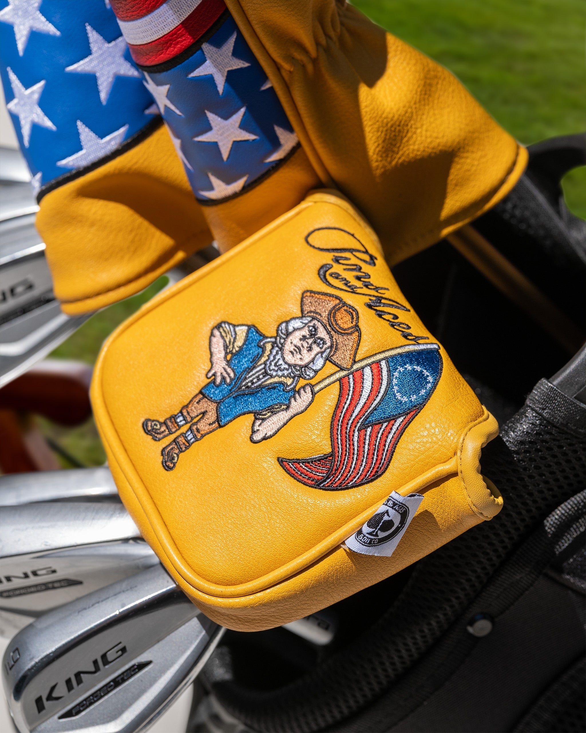 Bold yellow mallet cover featuring a patriotic design with a character holding an American flag, perfect for golf enthusiasts.