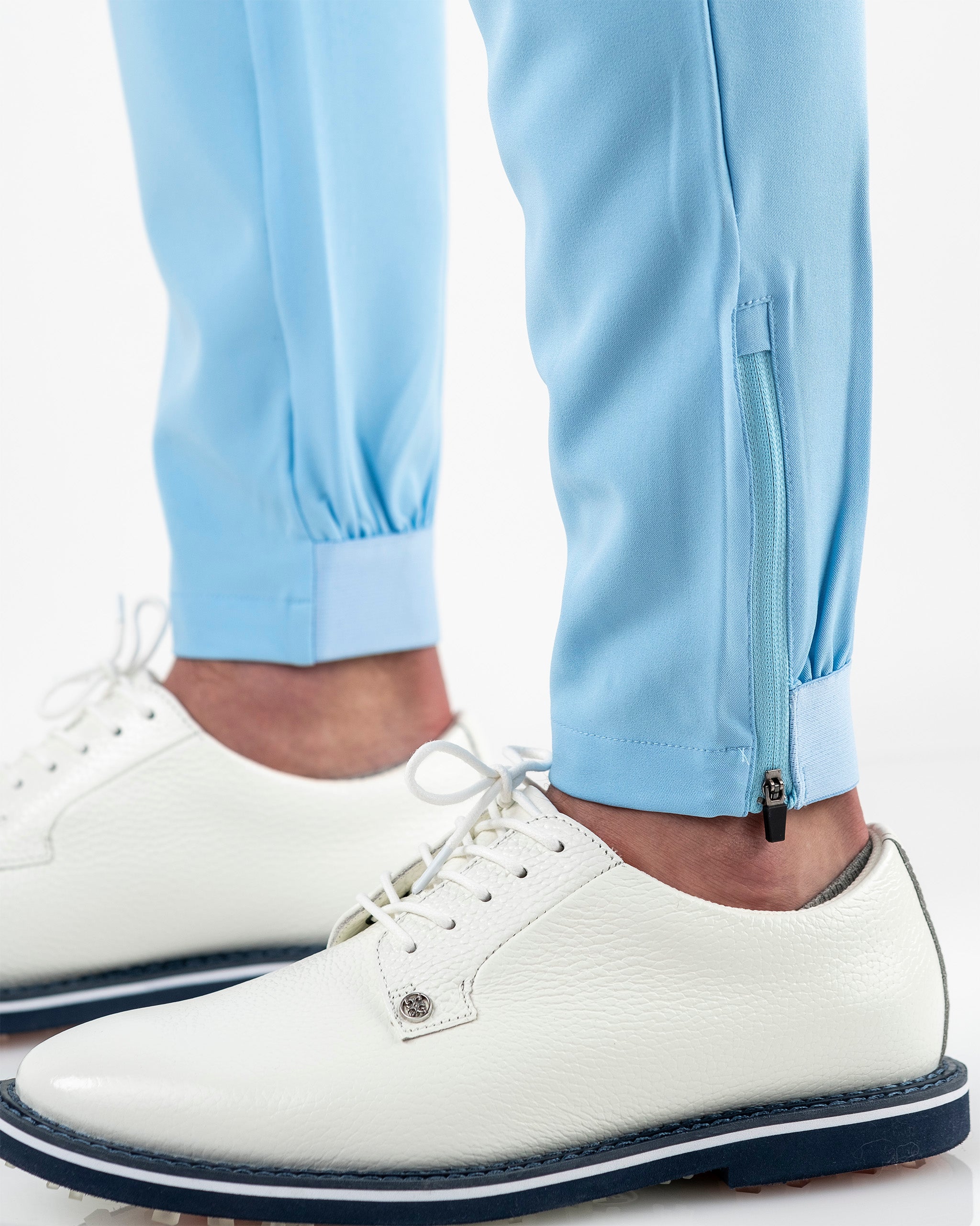 Sky blue performance jogger with zippered cuffs, paired with stylish white golf shoes for a modern look on the course.