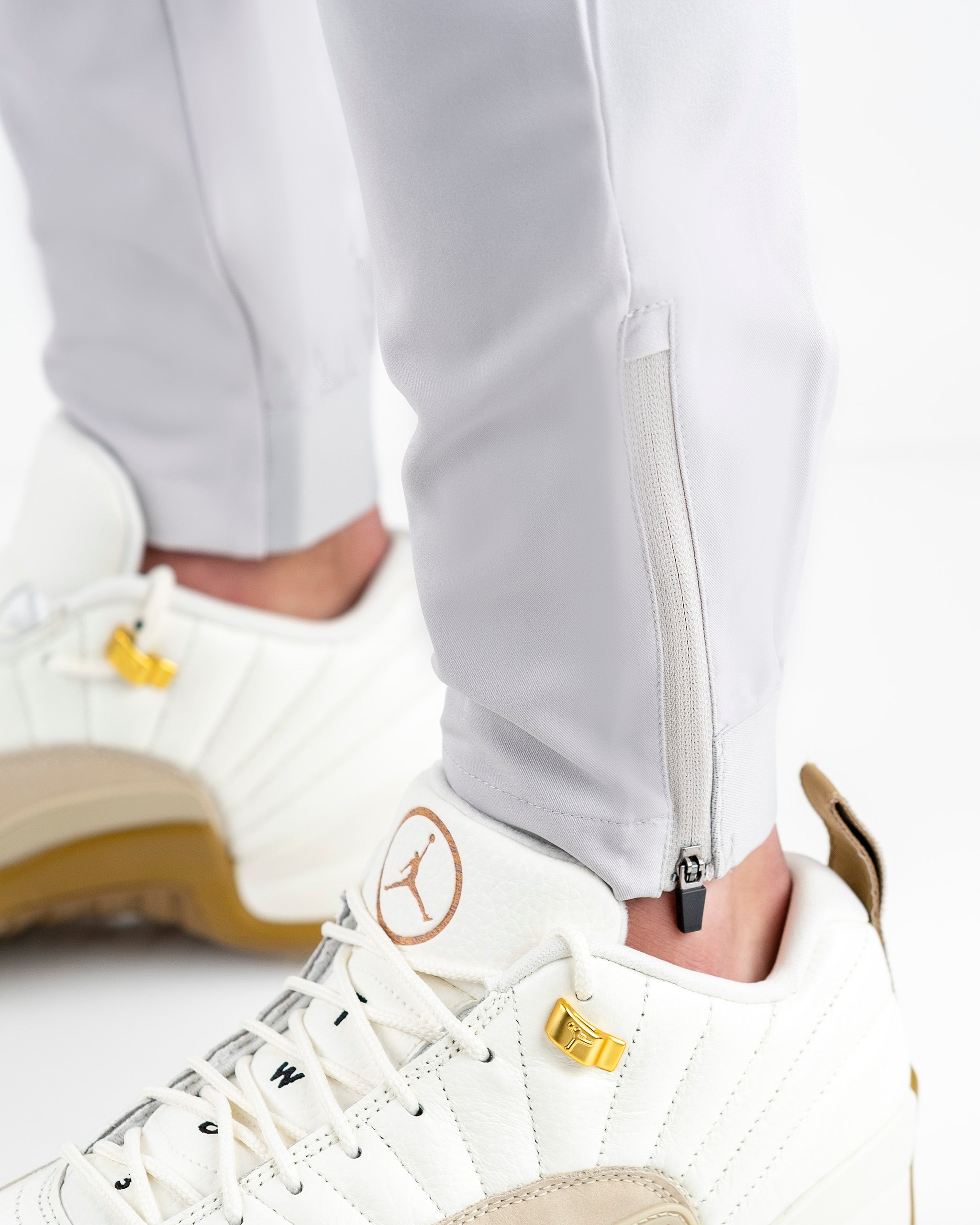 Performance jogger in stone color featuring zippered cuffs, paired with stylish white sneakers for a modern athletic look.