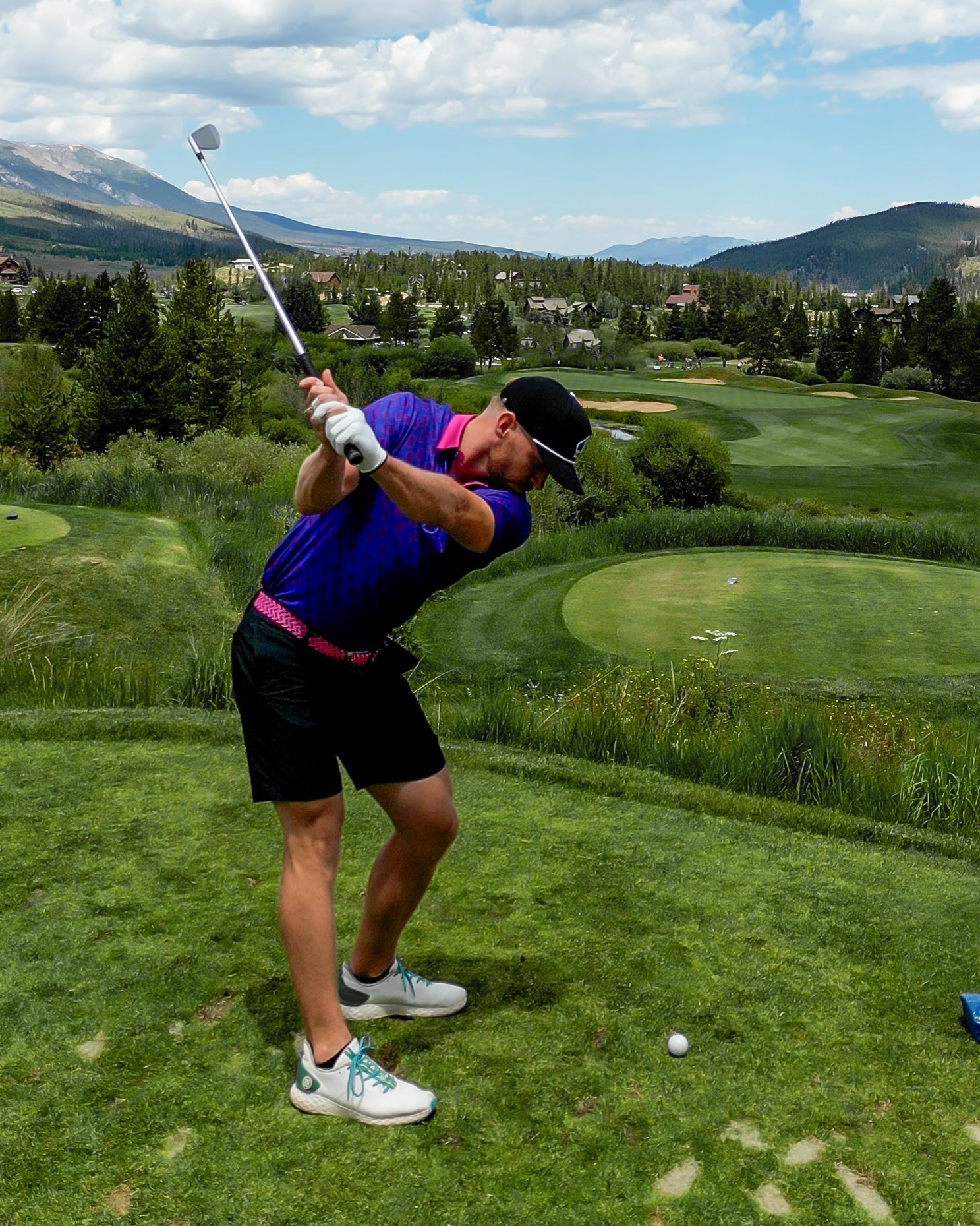 A golfer swings on the course, wearing a pink Pins Belt with a vibrant purple shirt and black shorts, showcasing bold style.