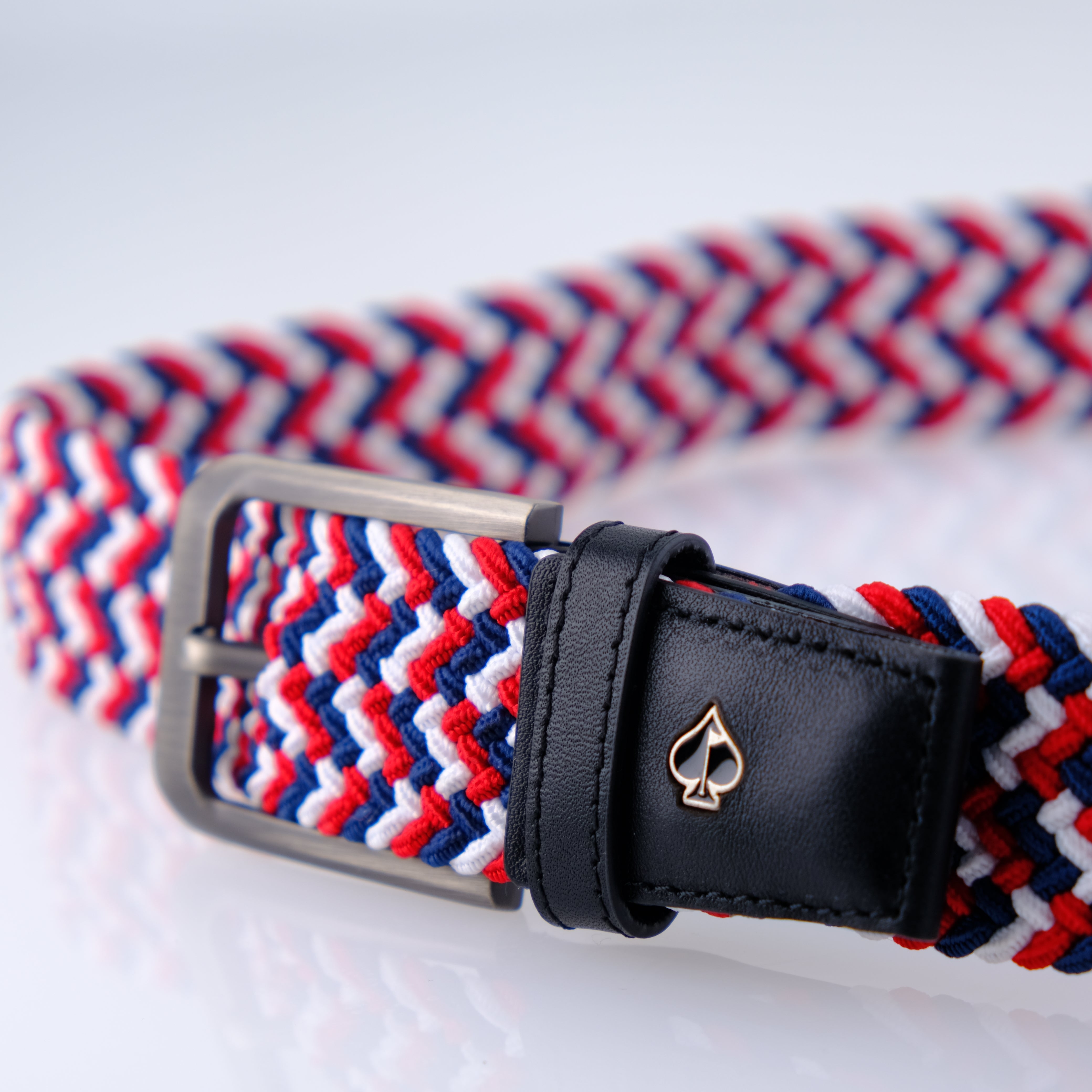 Woven red, white, and blue belt with a sleek black leather buckle featuring a gold spade logo. Ideal for stylish golfers.