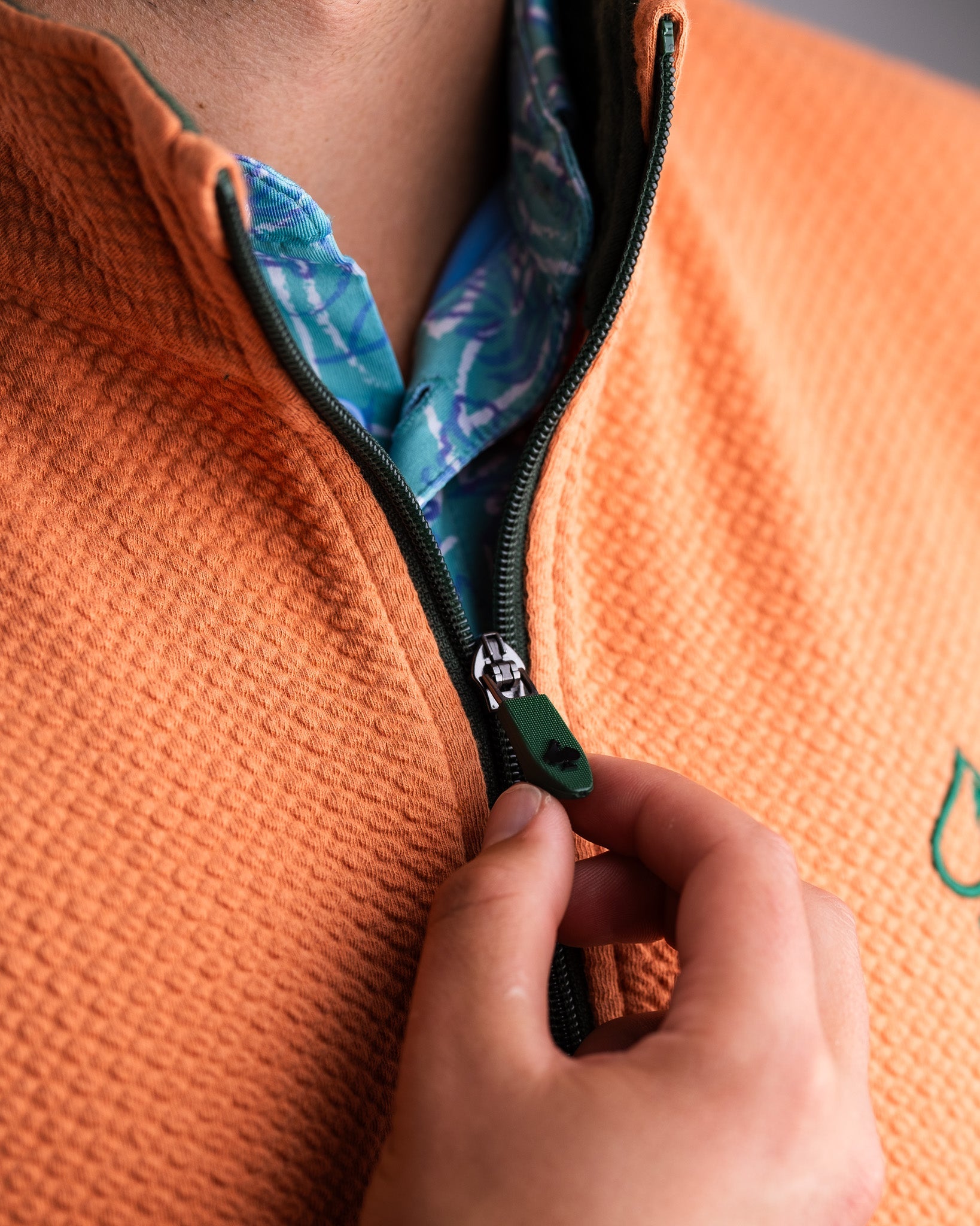 Close-up of a person zipping up a pumpkin-colored waffle knit pullover, showcasing its textured fabric and style.