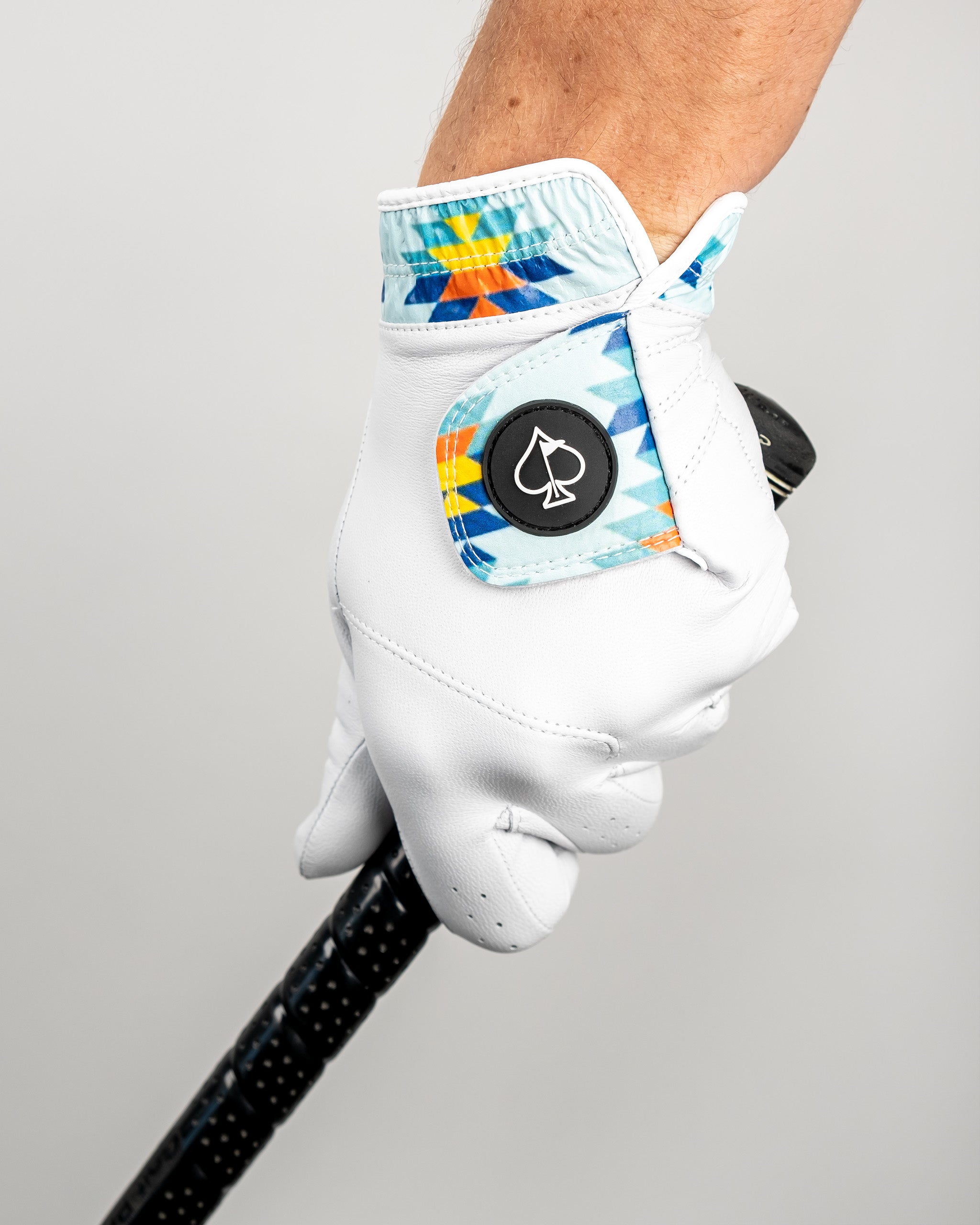Premium Tour Glove in Southwest Sunset design, featuring vibrant colors and a stylish pattern, held by a golfer gripping a club.