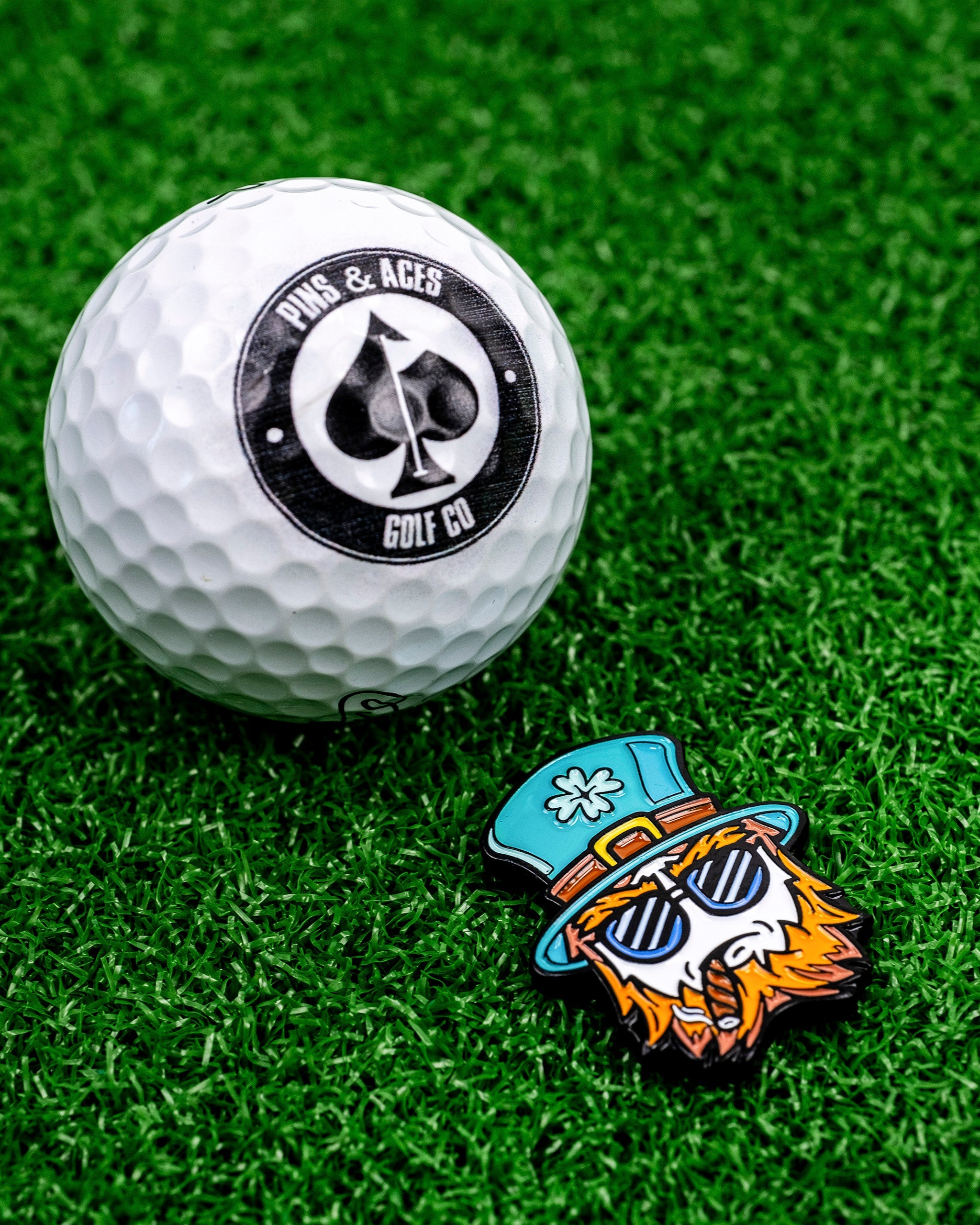Seamus the Degenerate Ball Marker features a colorful leprechaun design next to a golf ball on green turf.